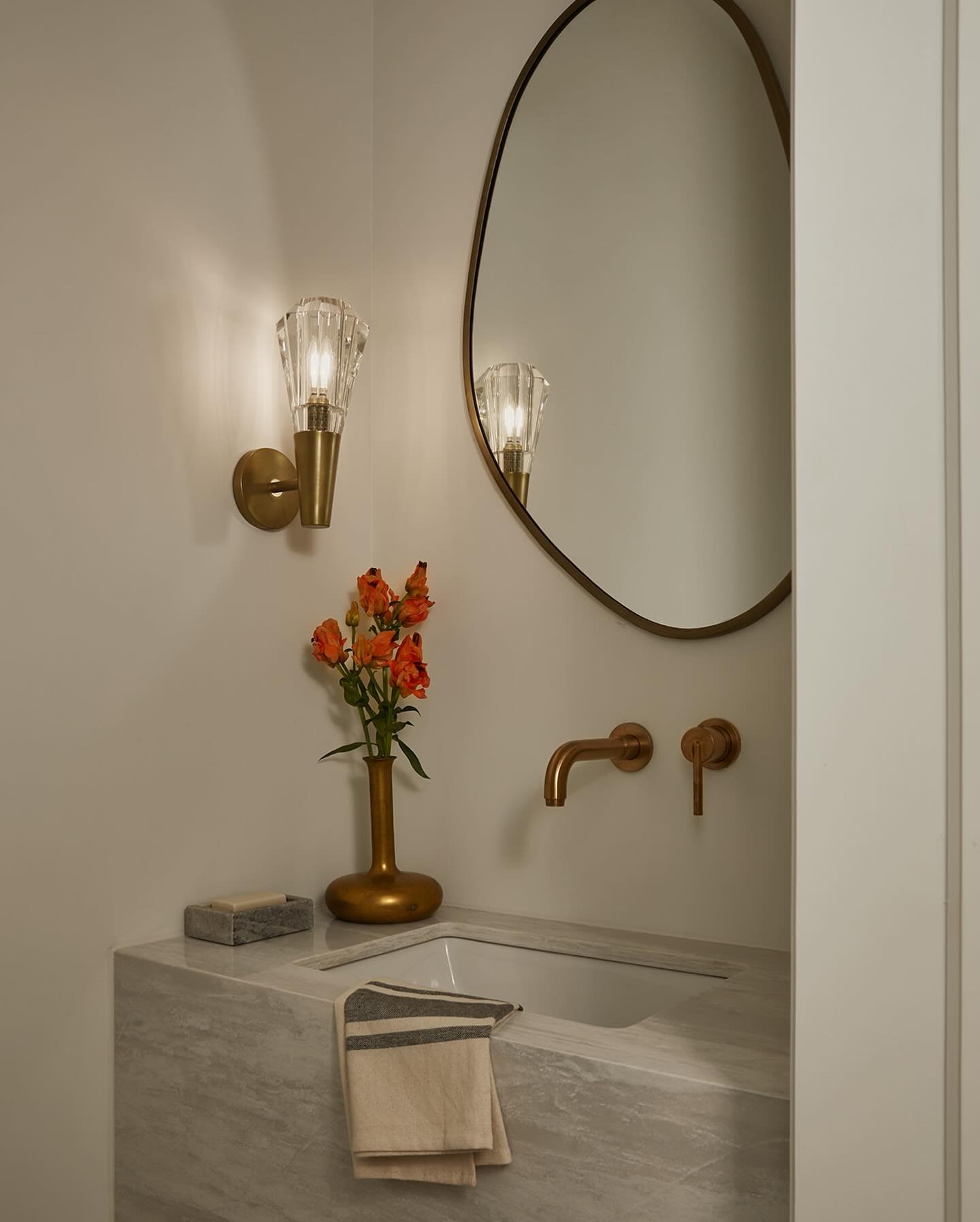 Modern powder room with a floating marble sink, brass wall-mounted faucet, and luxurious fluted crystal sconces.