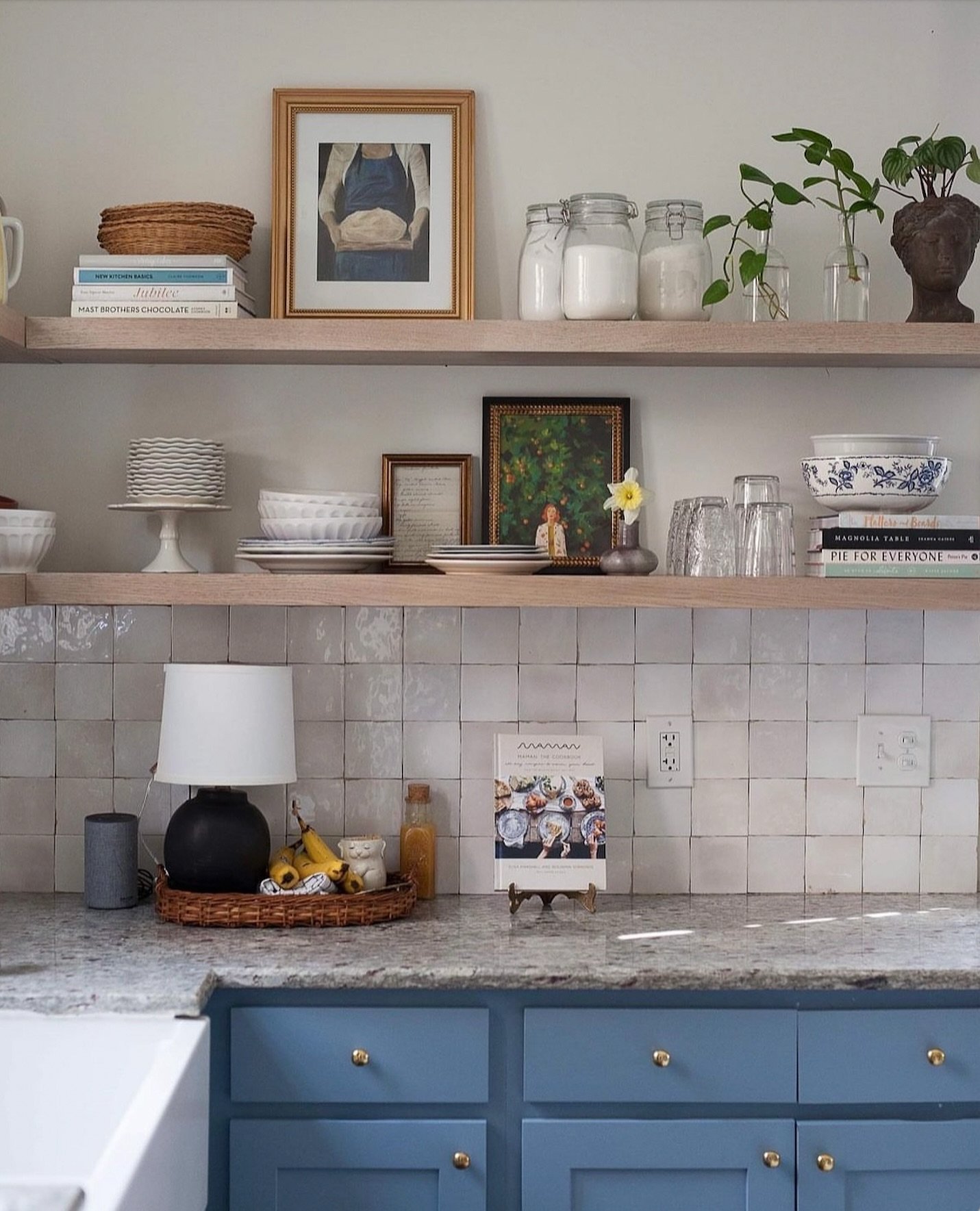 A textured, framed textile or fiber art piece hanging above a small kitchen side table with plants.