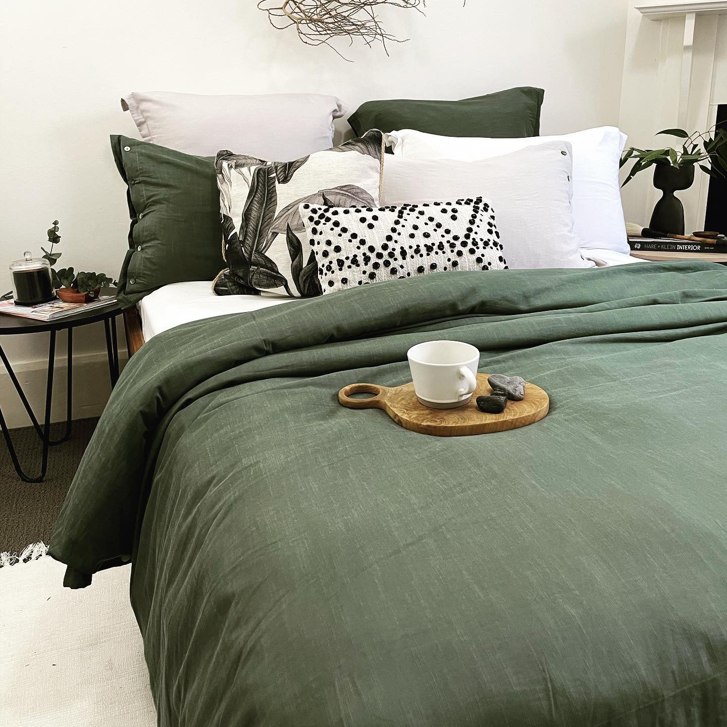 A modern bed with an olive green duvet cover, styled with a mix of black and white patterned throw pillows.