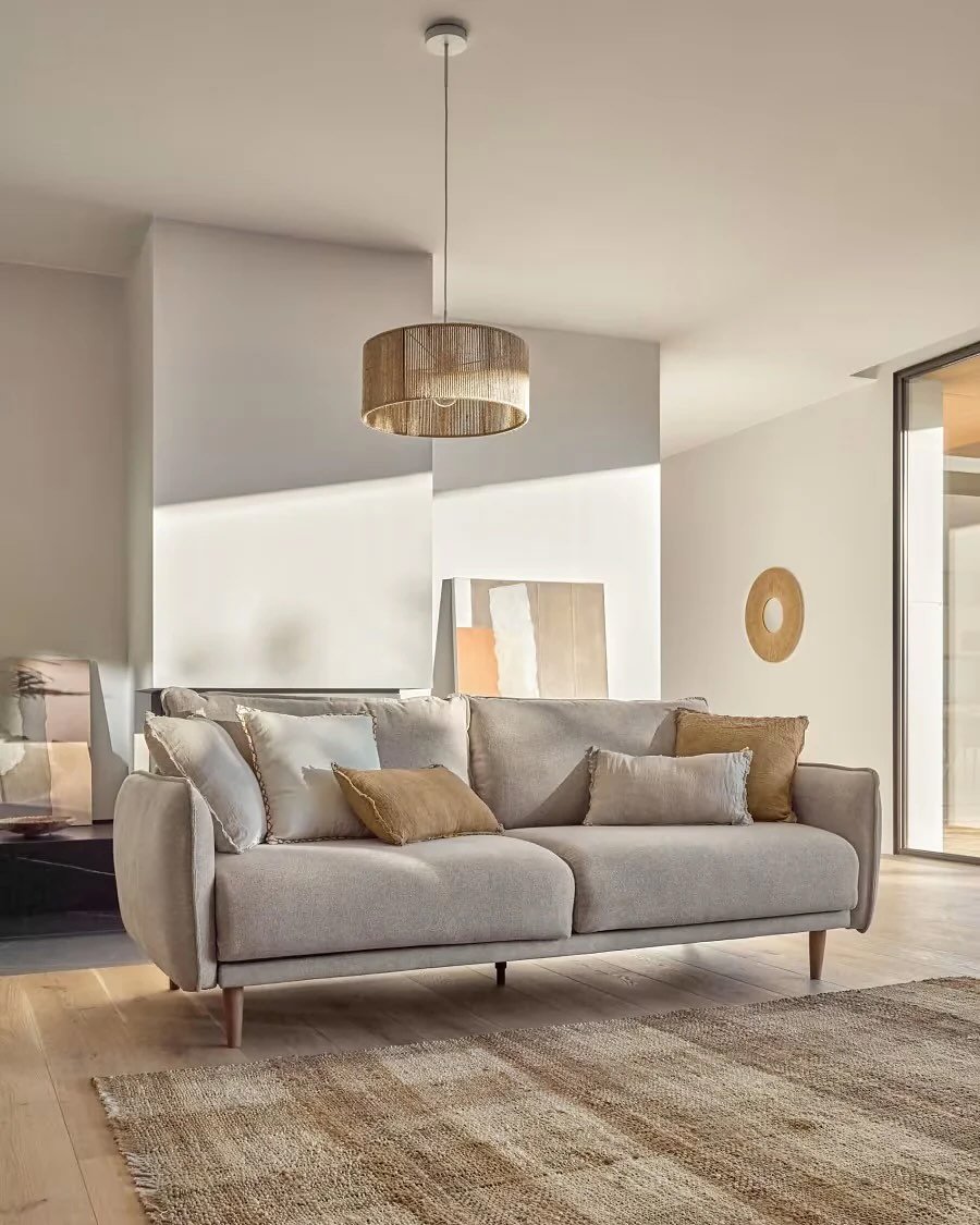 A bright, contemporary living room with a neutral greige sofa, a round jute area rug, and a cylindrical woven pendant light.