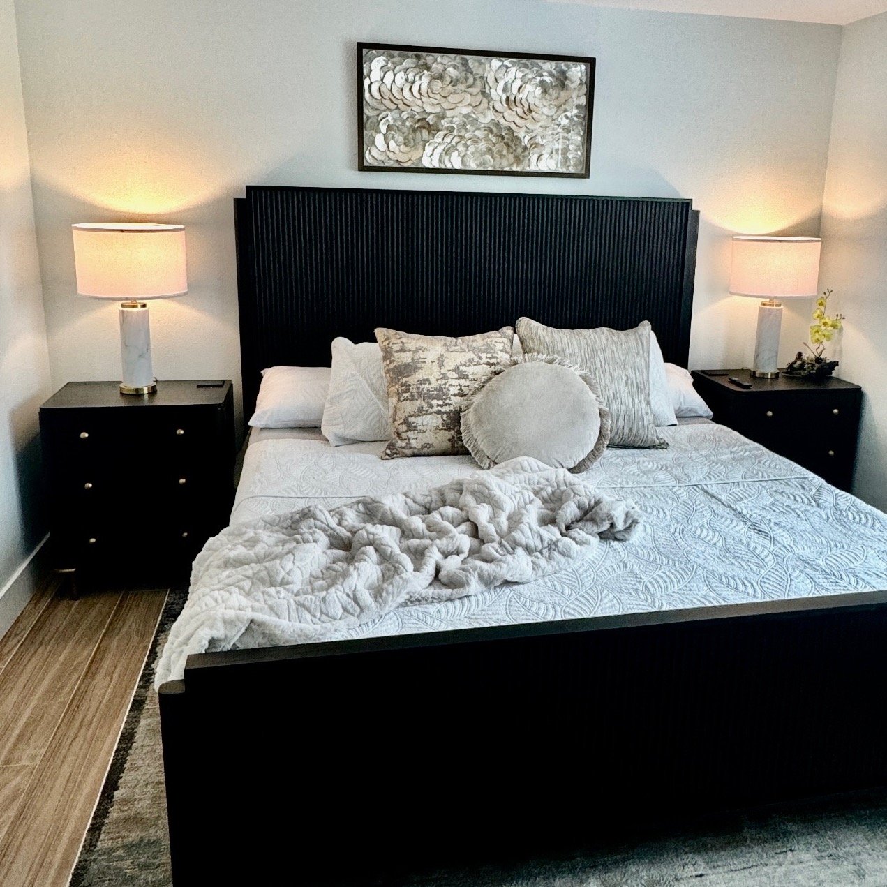 Pair of three-drawer black nightstands with small brass knobs flanking a black fluted headboard and bed frame.