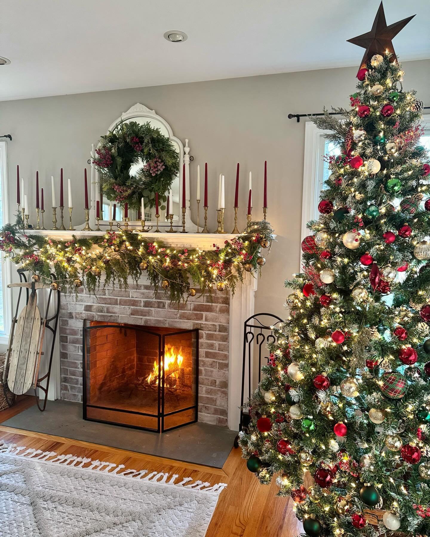 Whitewashed brick fireplace mantel decorated with a red berry garland, an assortment of tall brass candlesticks, and a round cranberry wreath above.