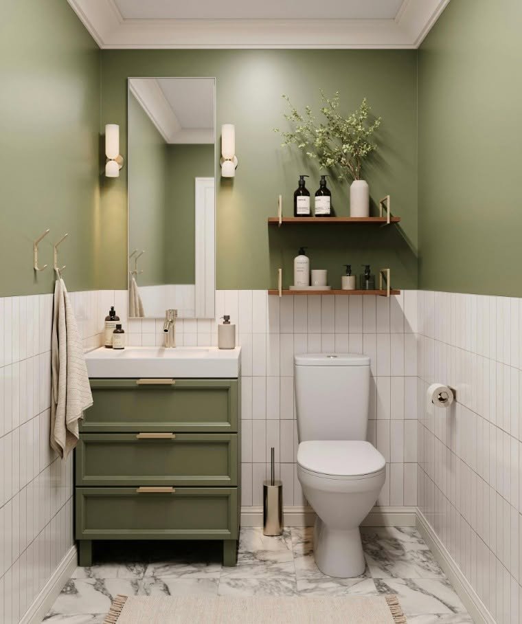 Two short, thin wood shelves with subtle gold brackets on an olive green wall, holding bottles and a vase of greenery next to a toilet.
