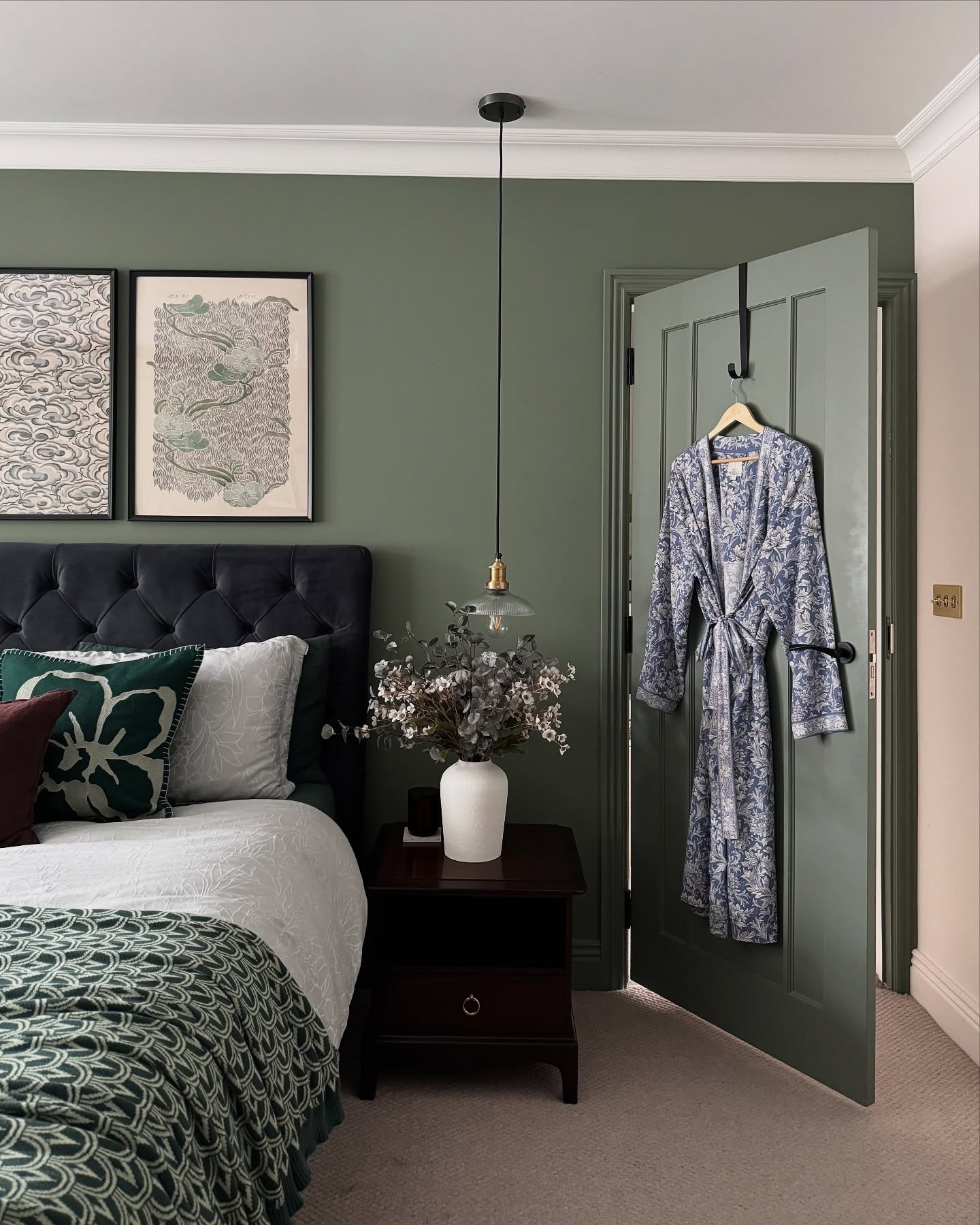 Bedroom with deep sage green walls and door, a navy velvet tufted headboard, and vintage-style framed artwork.