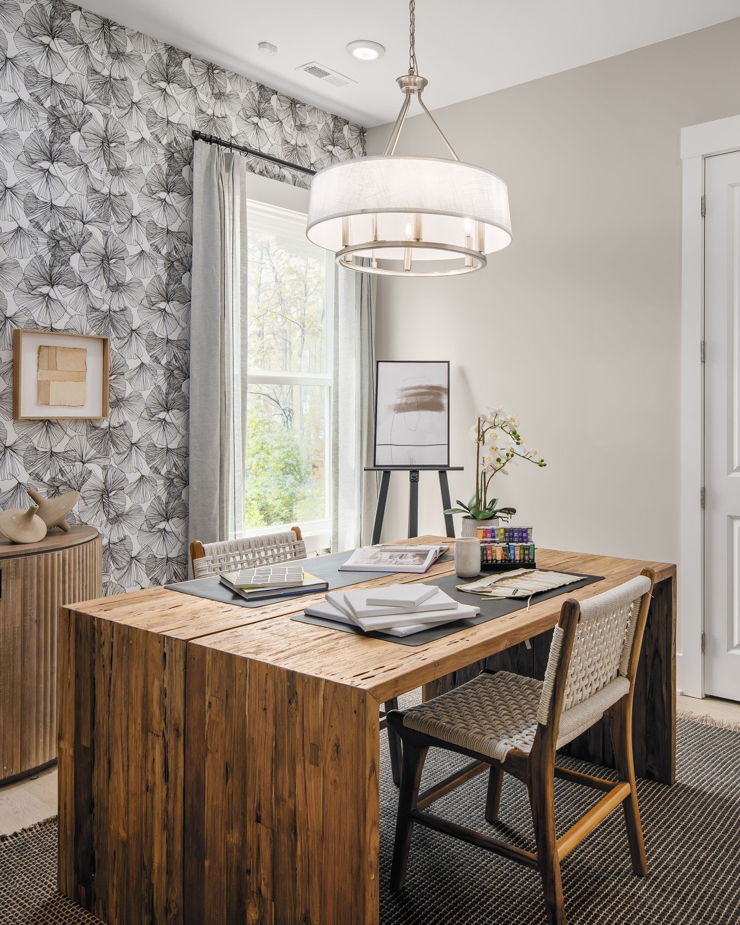 Home office with a black and white graphic wallpaper accent wall, a rough wood block desk, and two woven rope chairs over a textured area rug.