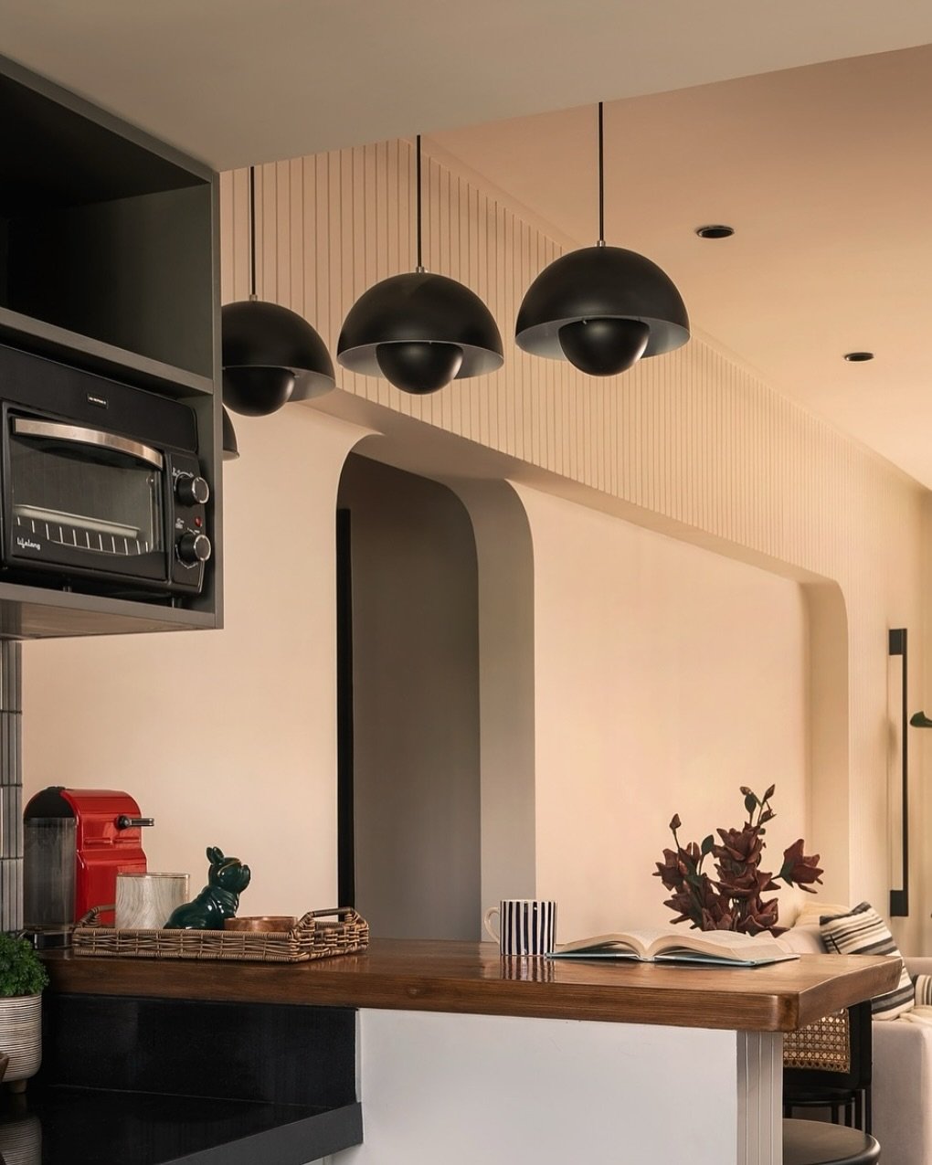 Three minimalistic, narrow brass rod pendants suspended over a light-colored kitchen island.