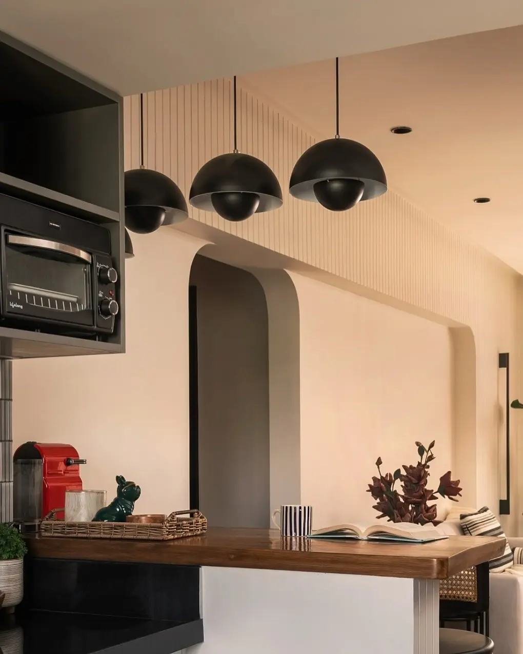 Three minimalistic, narrow brass rod pendants suspended over a light-colored kitchen island.