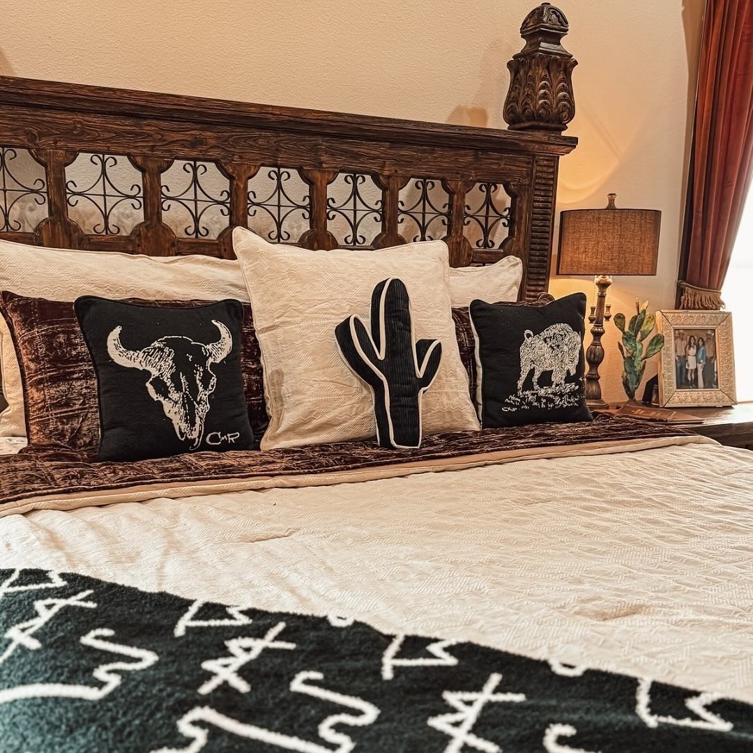 Close-up of a carved dark wood headboard with wrought iron details and a bed dressed with customized Western-themed throw pillows.