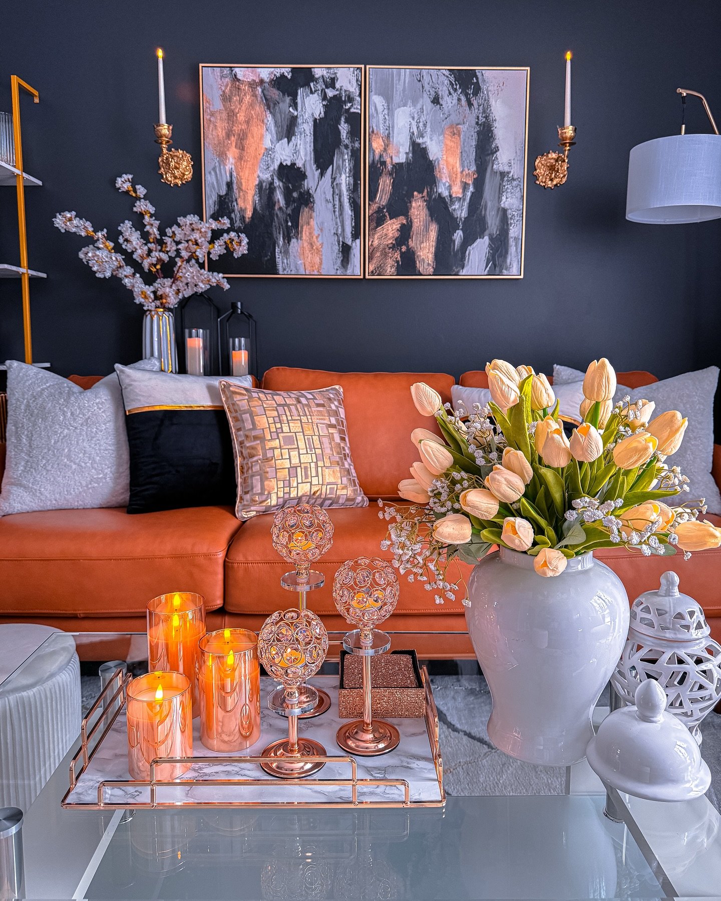 Two-panel abstract diptych painting with black, grey, and metallic copper strokes, framed and hung above a brown leather sofa on a dark grey wall.