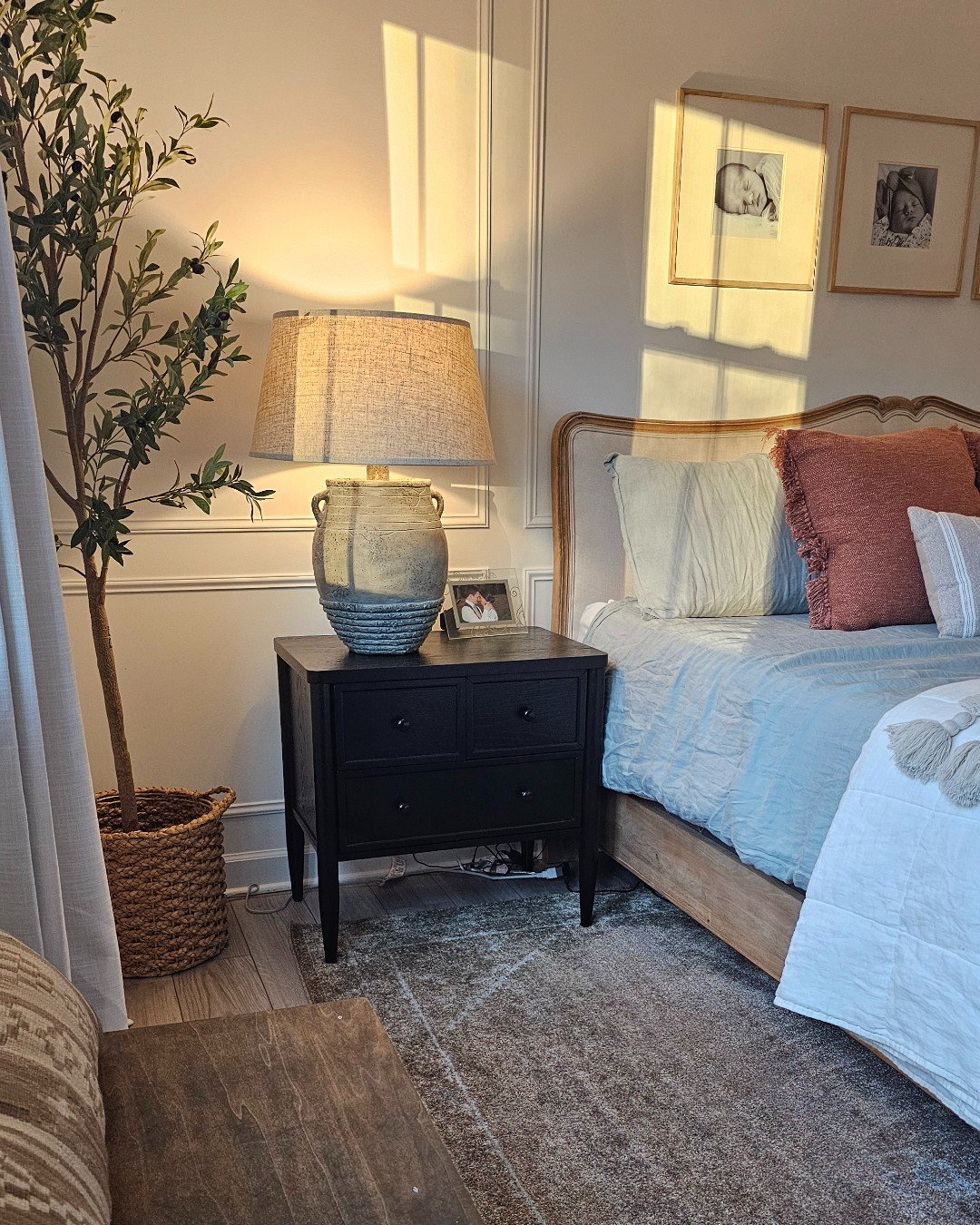 Small, matte black nightstand with two drawers and two small knobs on each drawer, beside a light blue bed.