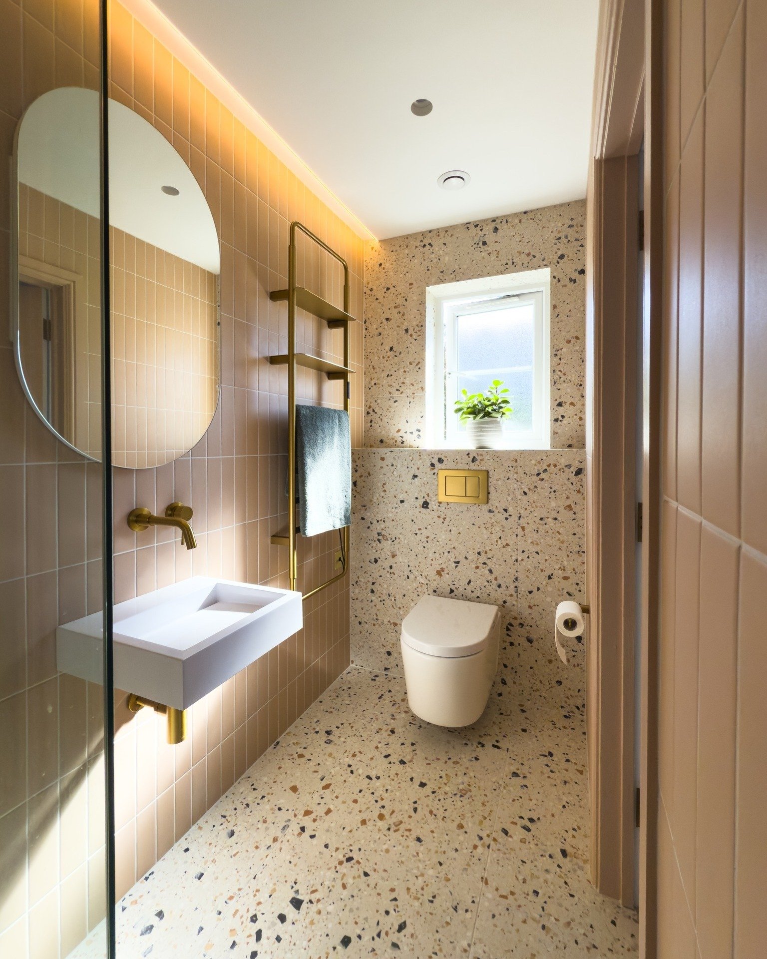 A small, modern bathroom with peach subway wall tiles and a floor and toilet wall covered in light beige terrazzo with black, brown, and terracotta-colored stone chips.
