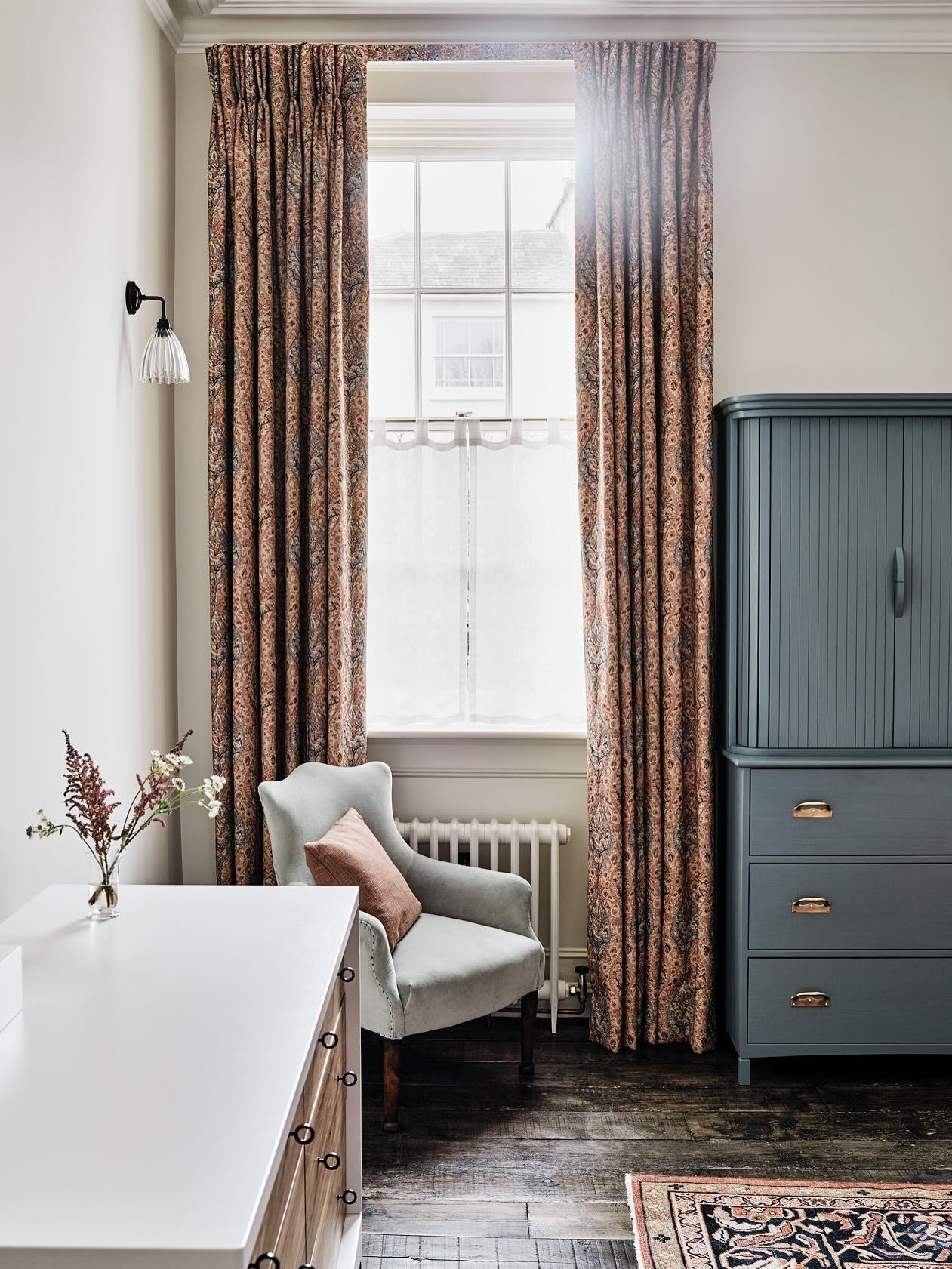 Rust and blue paisley print pinch-pleat curtains framing a window with a lace cafe curtain.