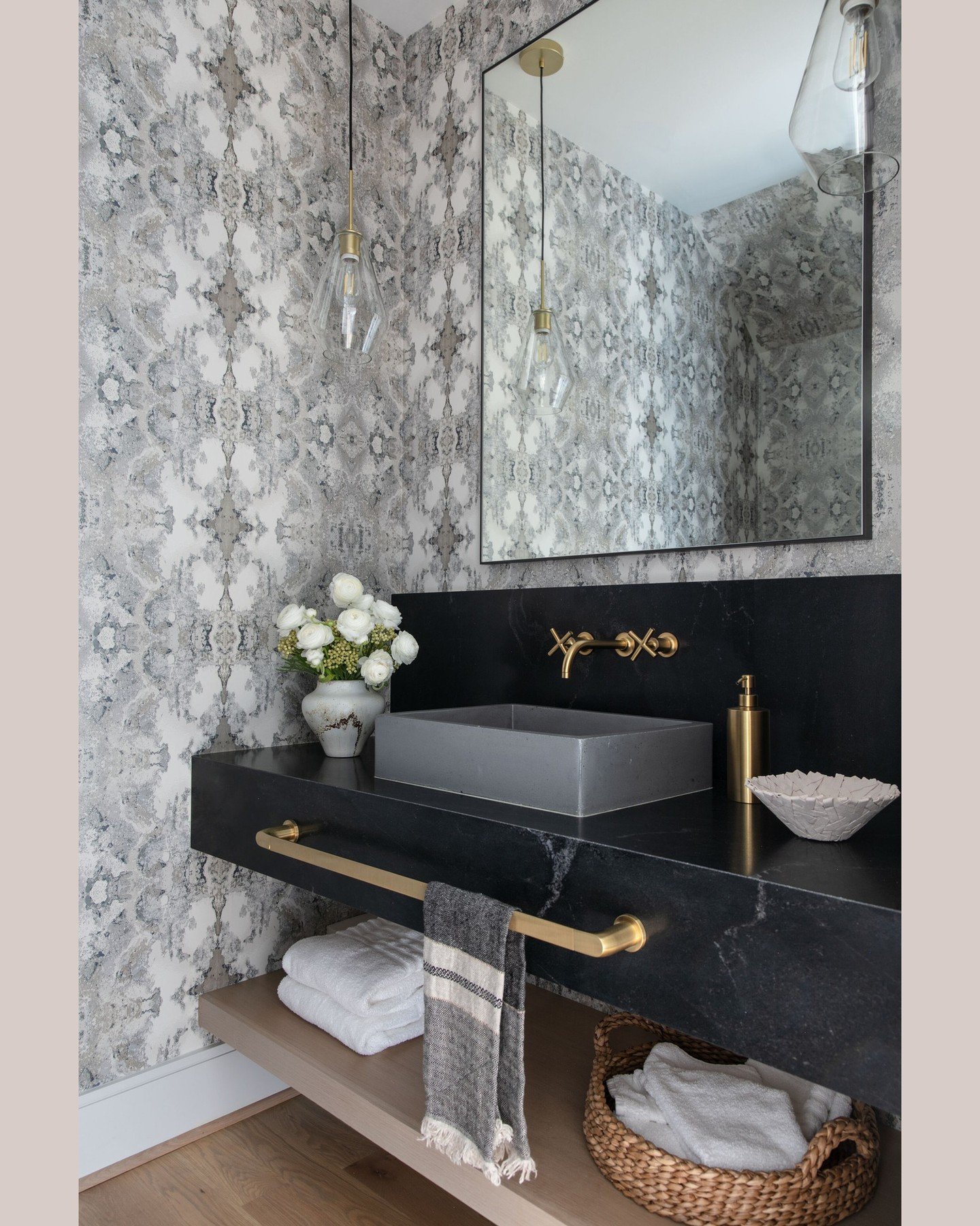 A long brass towel bar integrated under the front edge of a black stone floating vanity, holding a striped hand towel.
