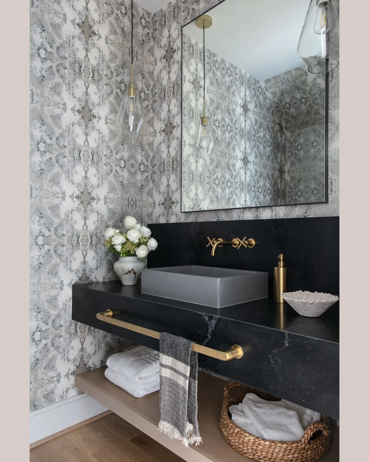 A long brass towel bar integrated under the front edge of a black stone floating vanity, holding a striped hand towel.