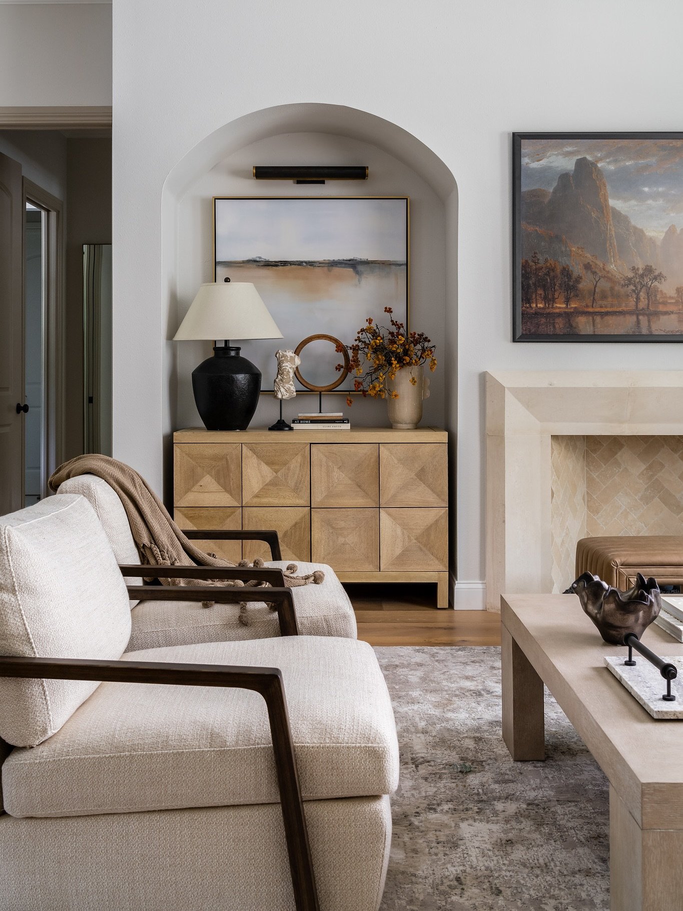 A close-up of a neutral living room with a cream armchair and a light wood cabinet placed within a recessed wall archway.