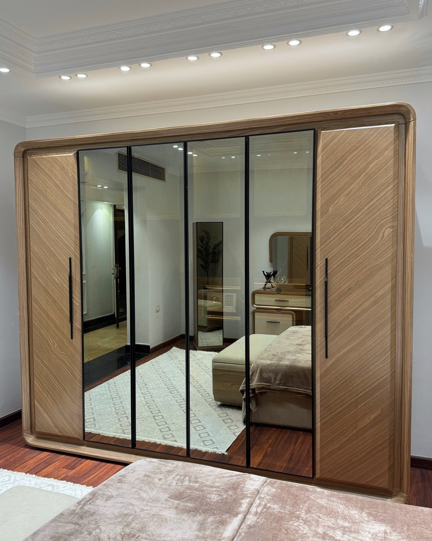 Large freestanding contemporary wardrobe with light wood veneer, rounded edges, and three central doors made of black-framed mirrored glass.