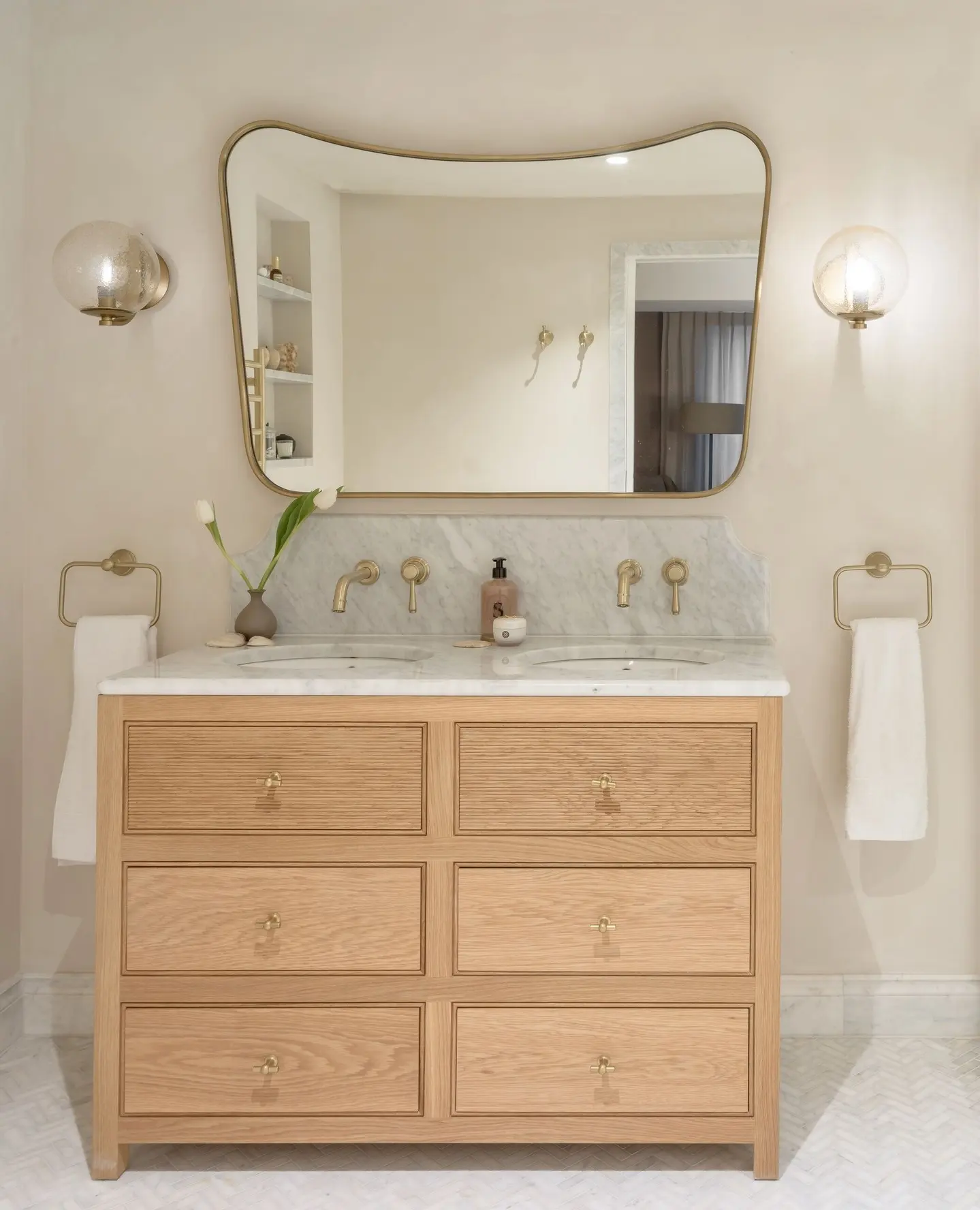 Two matching brass towel rings mounted on either side of a light wood double vanity, each holding a white hand towel.