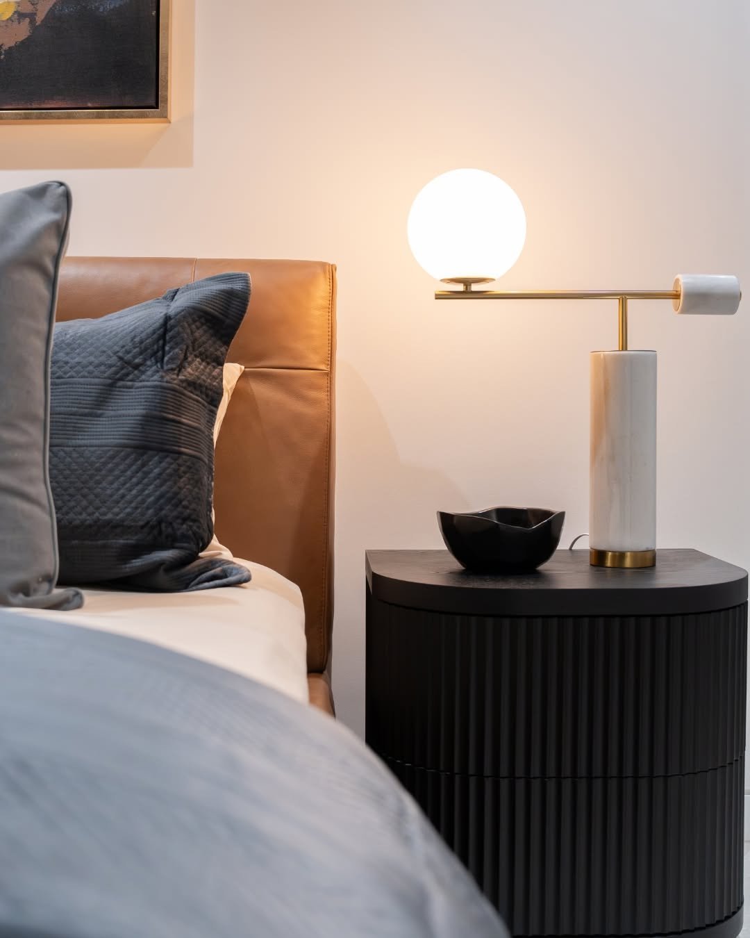 Black half-moon shaped nightstand with vertical fluting on the drawer fronts, topped with a modern globe and marble lamp.