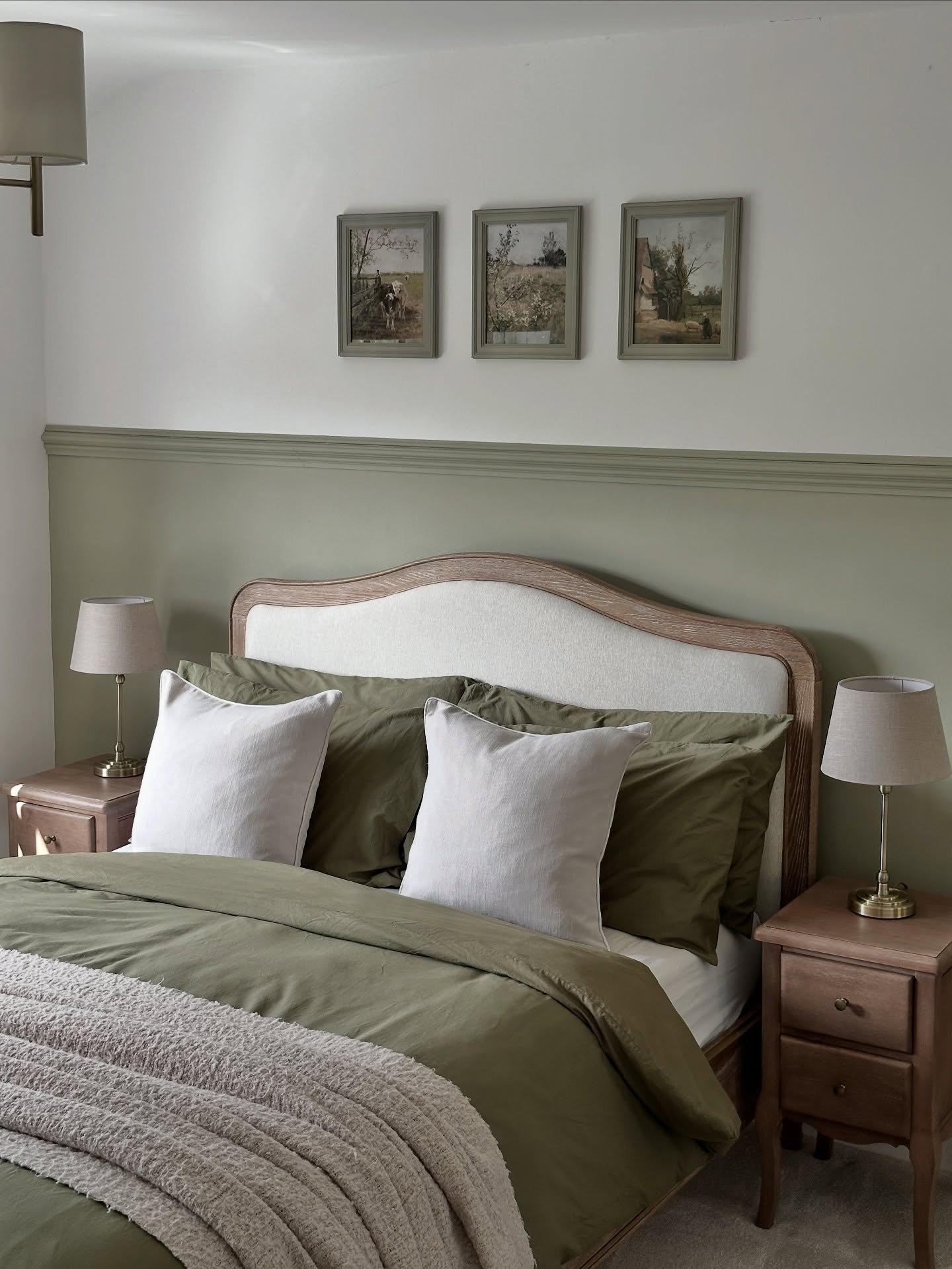 A cozy bedroom with an olive green half-wall, a bed with matching olive green bedding, and a light wood upholstered headboard.