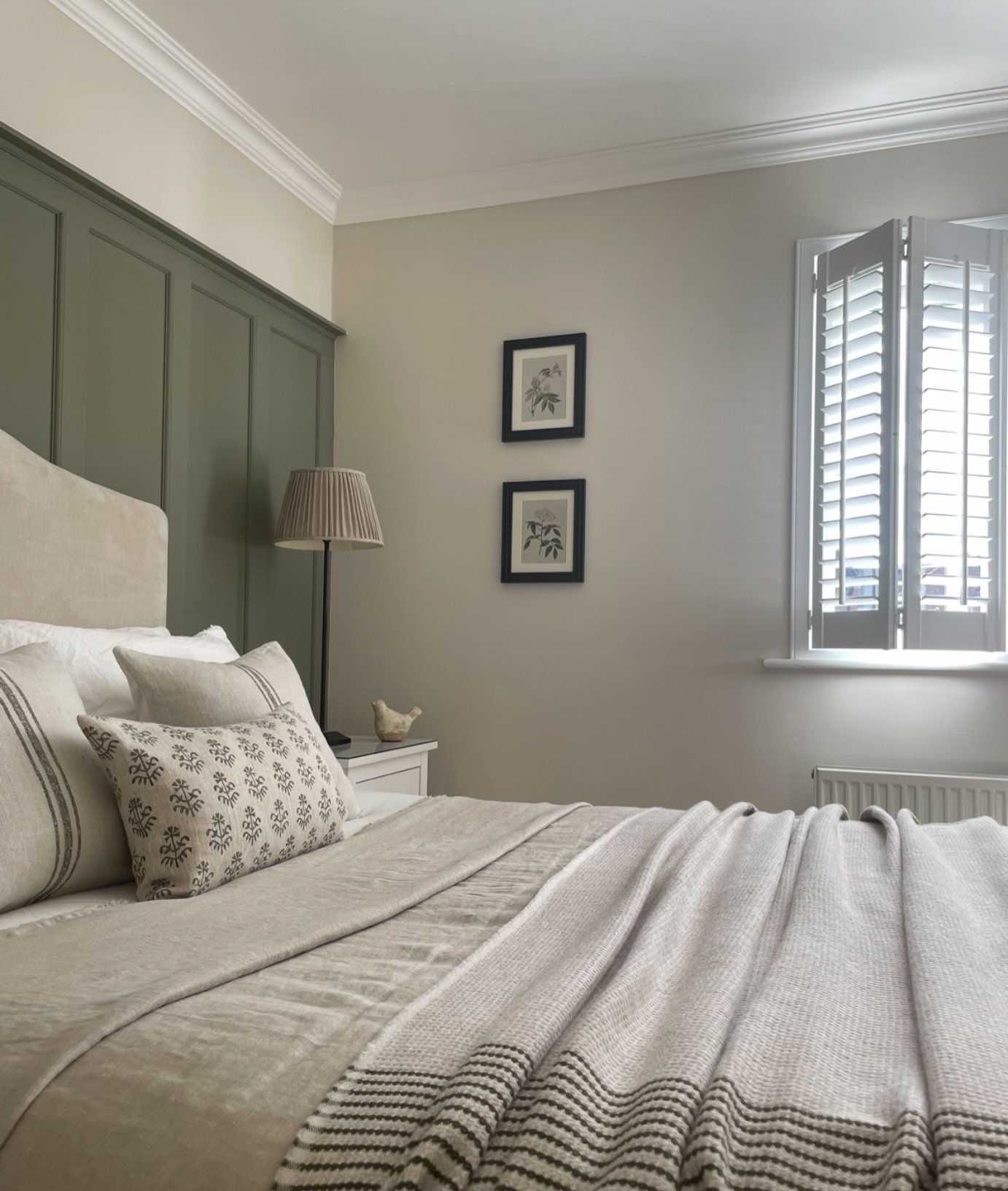 Bedroom featuring a deep sage green paneled accent wall, a neutral upholstered headboard, and layered linen bedding.