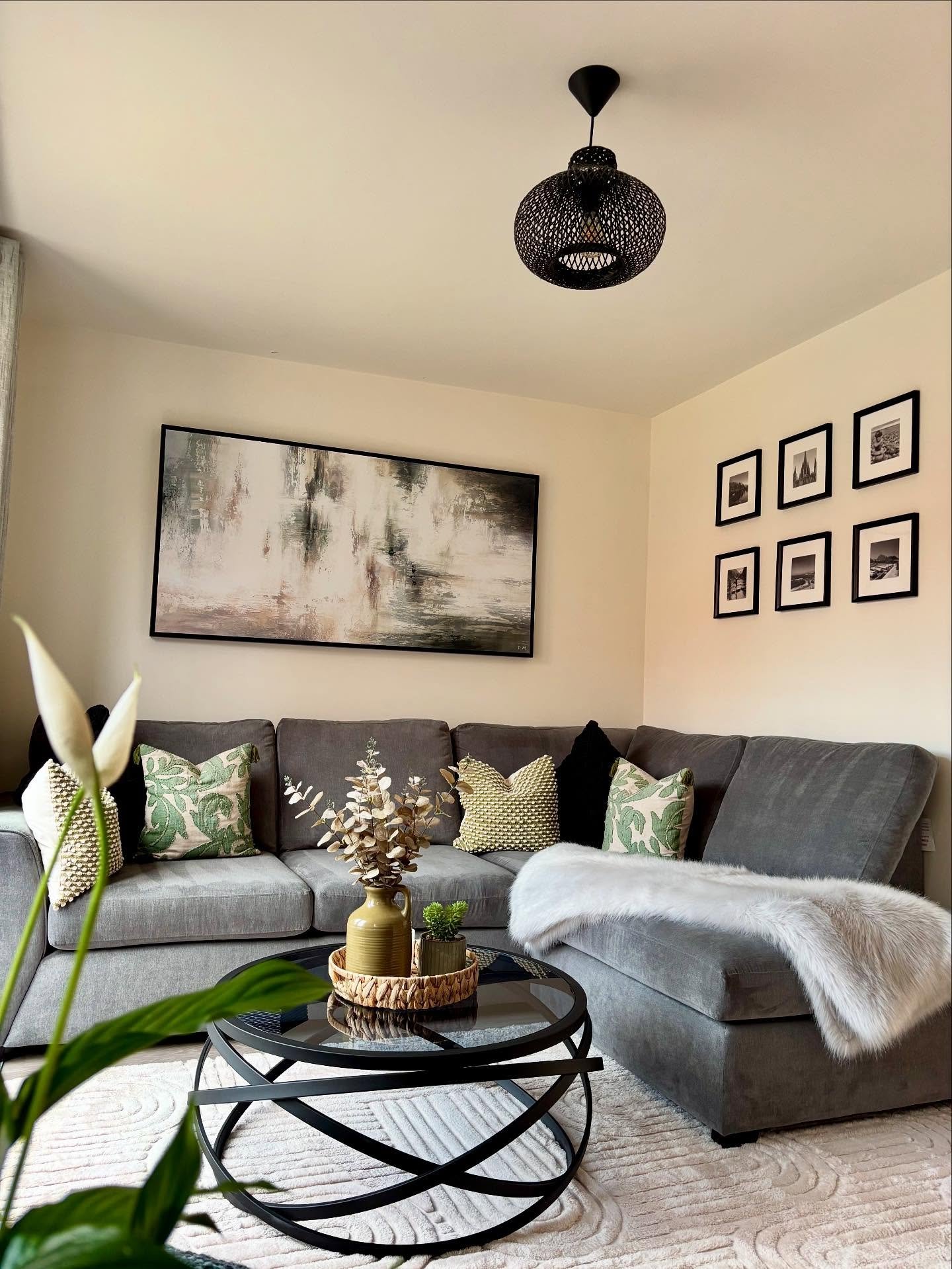 Very large horizontal abstract painting in muted greens, greys, and creams, framed in black and hung above a dark grey sectional sofa.