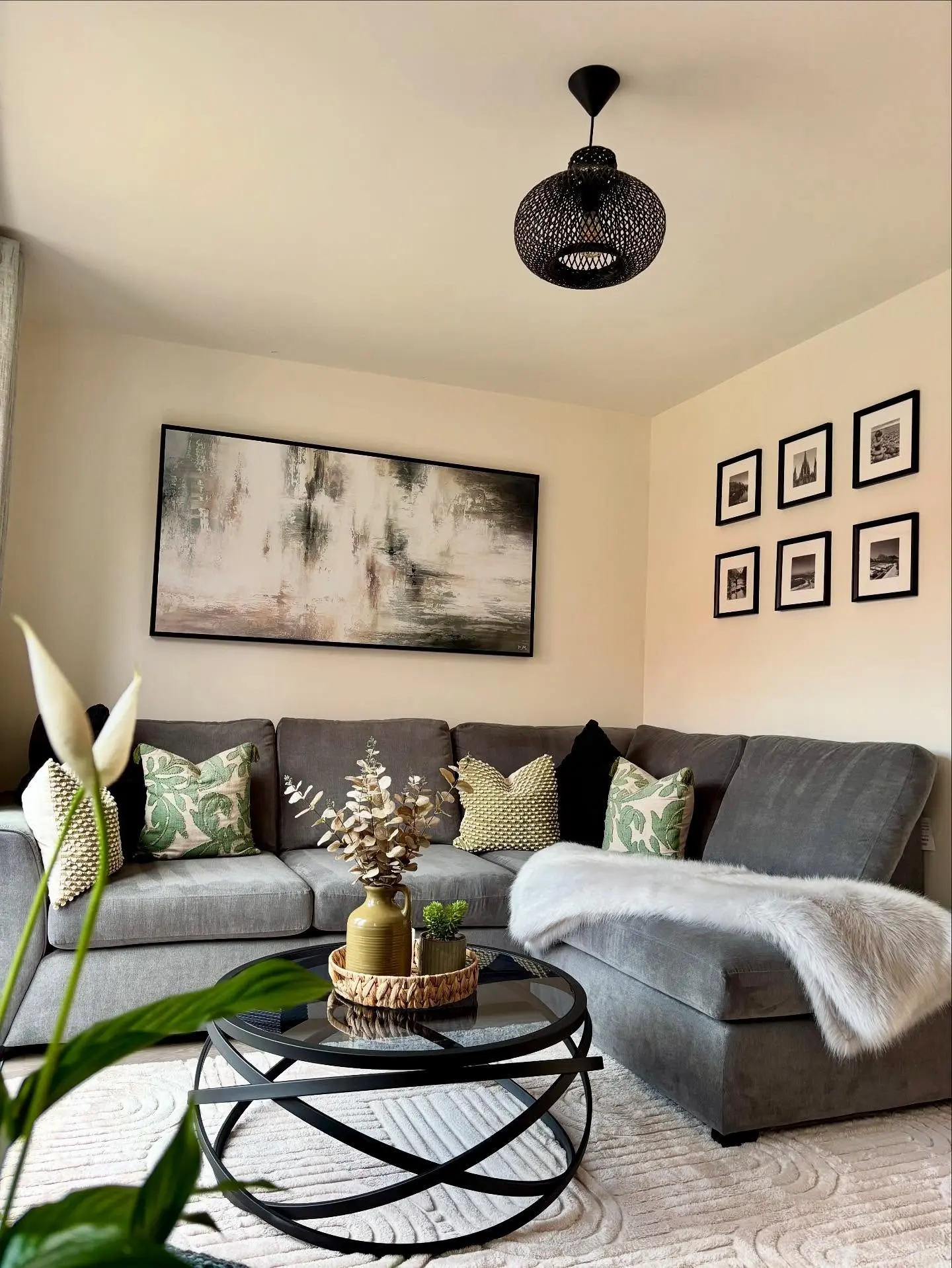 Very large horizontal abstract painting in muted greens, greys, and creams, framed in black and hung above a dark grey sectional sofa.