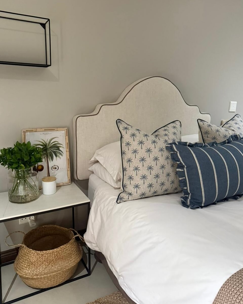 Medium-height, upholstered headboard featuring a stylized, arched profile reminiscent of a keyhole shape, covered in neutral linen with thin brown piping.