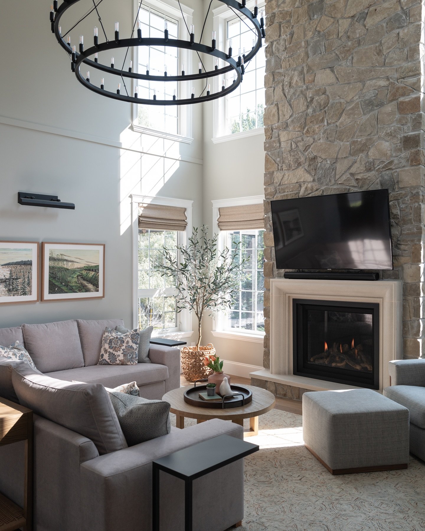 Two-story living room with a massive floor-to-ceiling natural stone fireplace, a large black circular chandelier, and a gray sectional sofa.