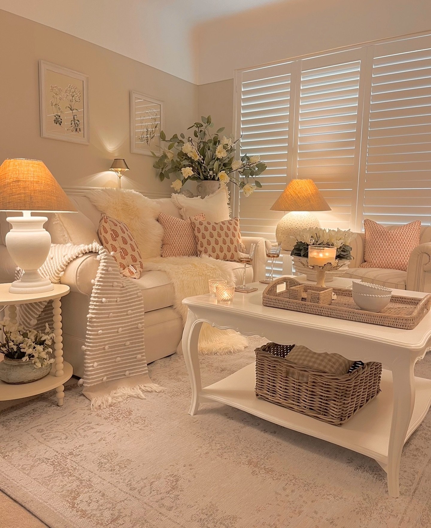 A cozy, heavily textured living room with a white sofa, a matching wood coffee table, and warm light from lamps with woven shades.