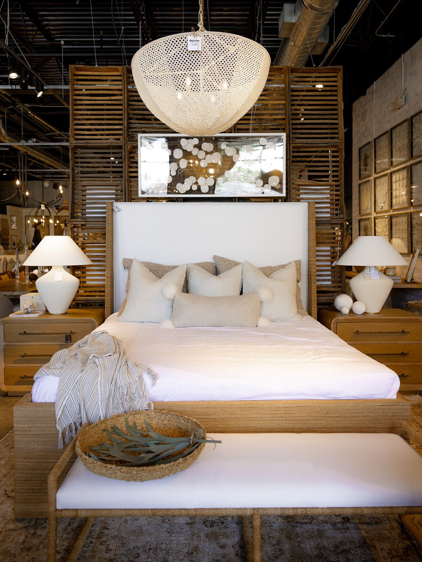A bedroom setting featuring a large bed with a woven jute frame, and a matching rectangular bench with a white upholstered cushion and woven base at the foot.