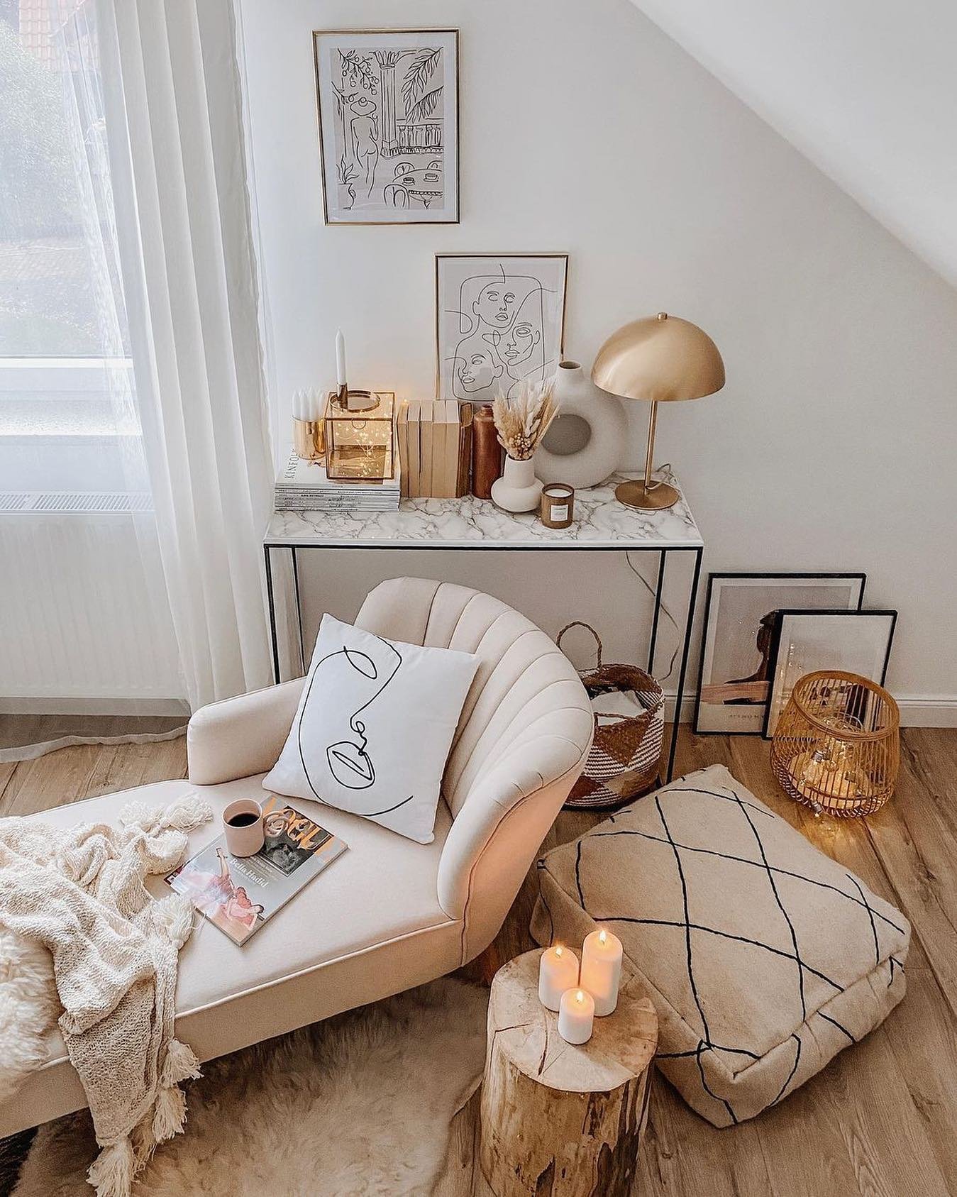 Light and bright reading corner with a velvet tufted chaise lounge, a marble console table, a large Moroccan pouf, and gold decor accents.