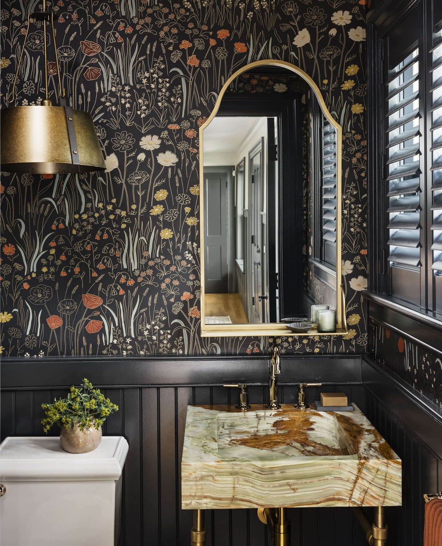 Powder room with black floral wallpaper, black beadboard wainscoting, and a vessel sink made from green and brown veined onyx.