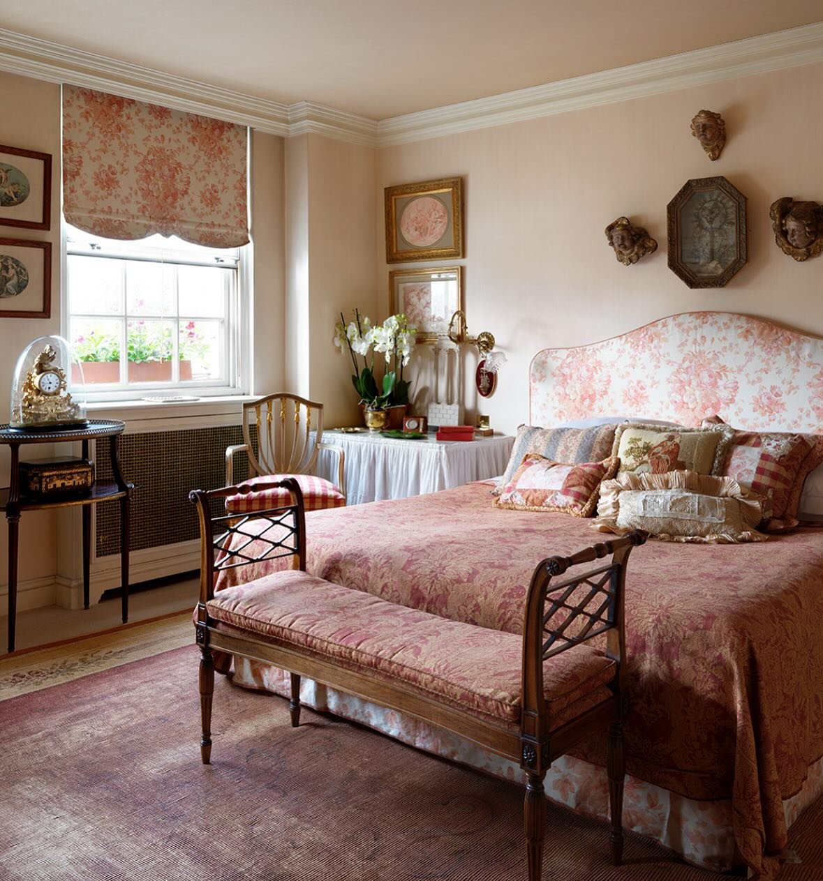 Traditional bedroom with floral chintz fabric on the headboard, Roman blind, and bedding, featuring antique furniture and wall decor.