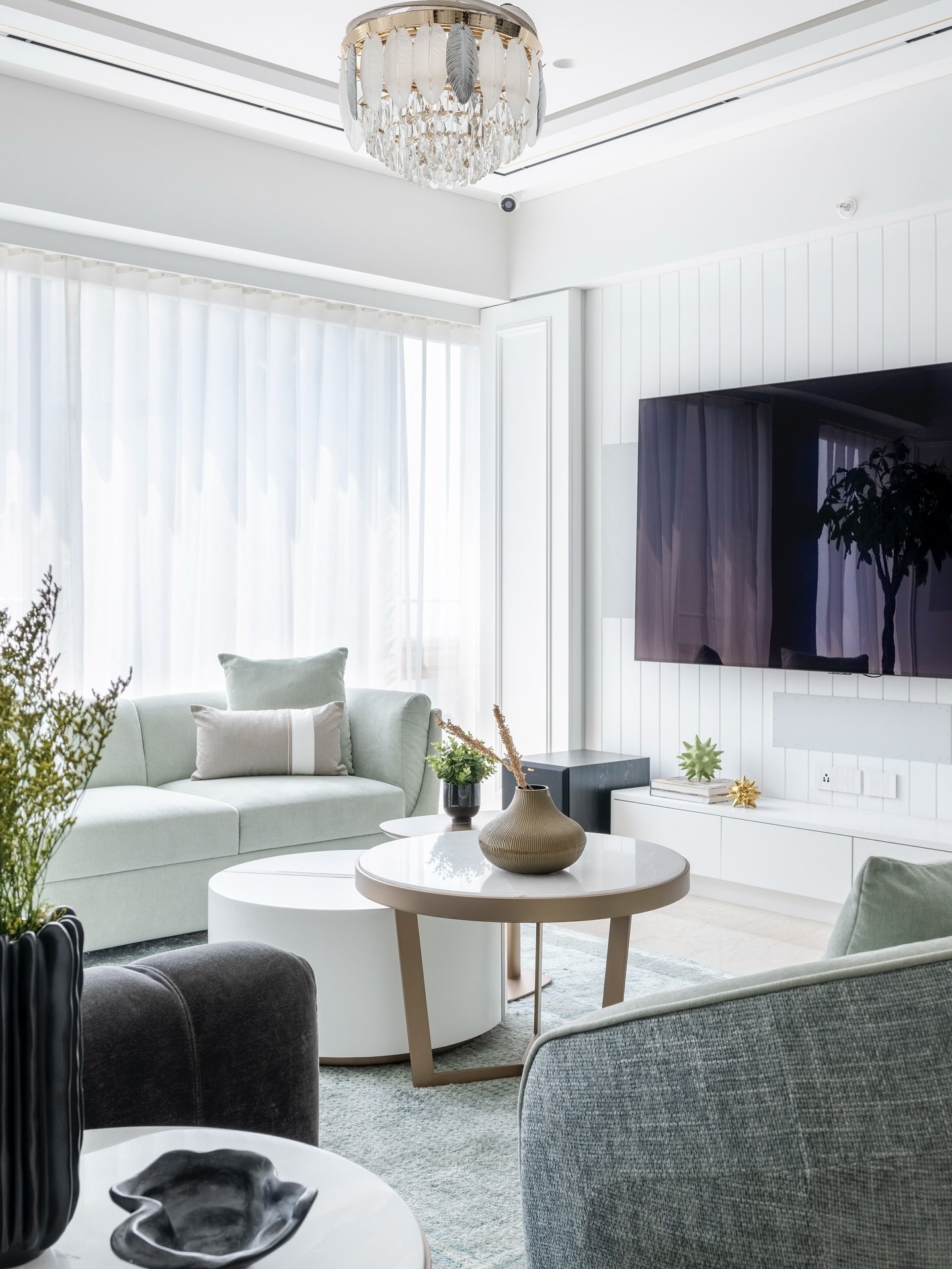 Bright living room with a mint green sofa, sheer curtains, white vertical paneling on the media wall, and layered round coffee tables.