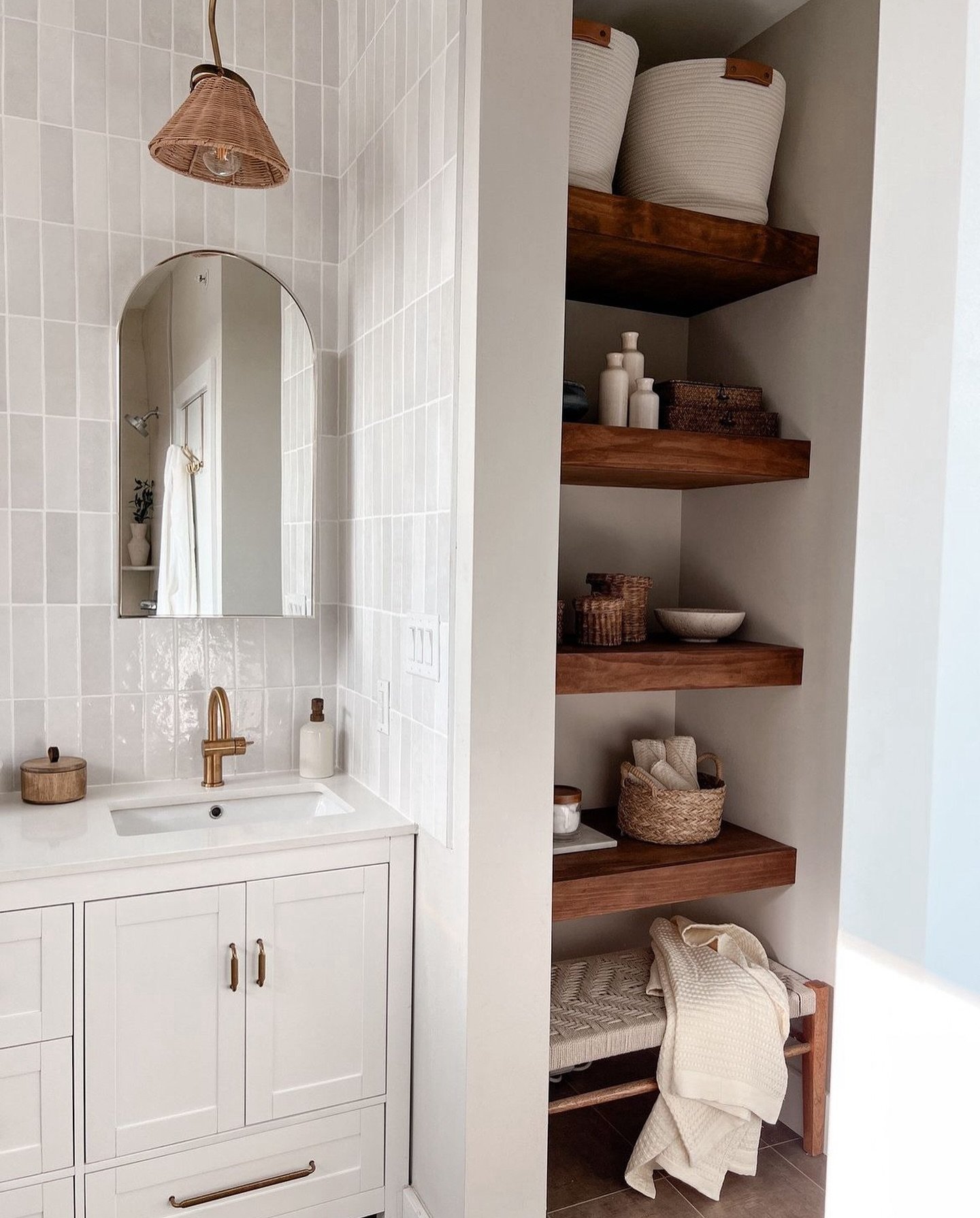 Four dark wood floating shelves installed within a wall niche, styled with woven baskets, small jars, and a low bench underneath.