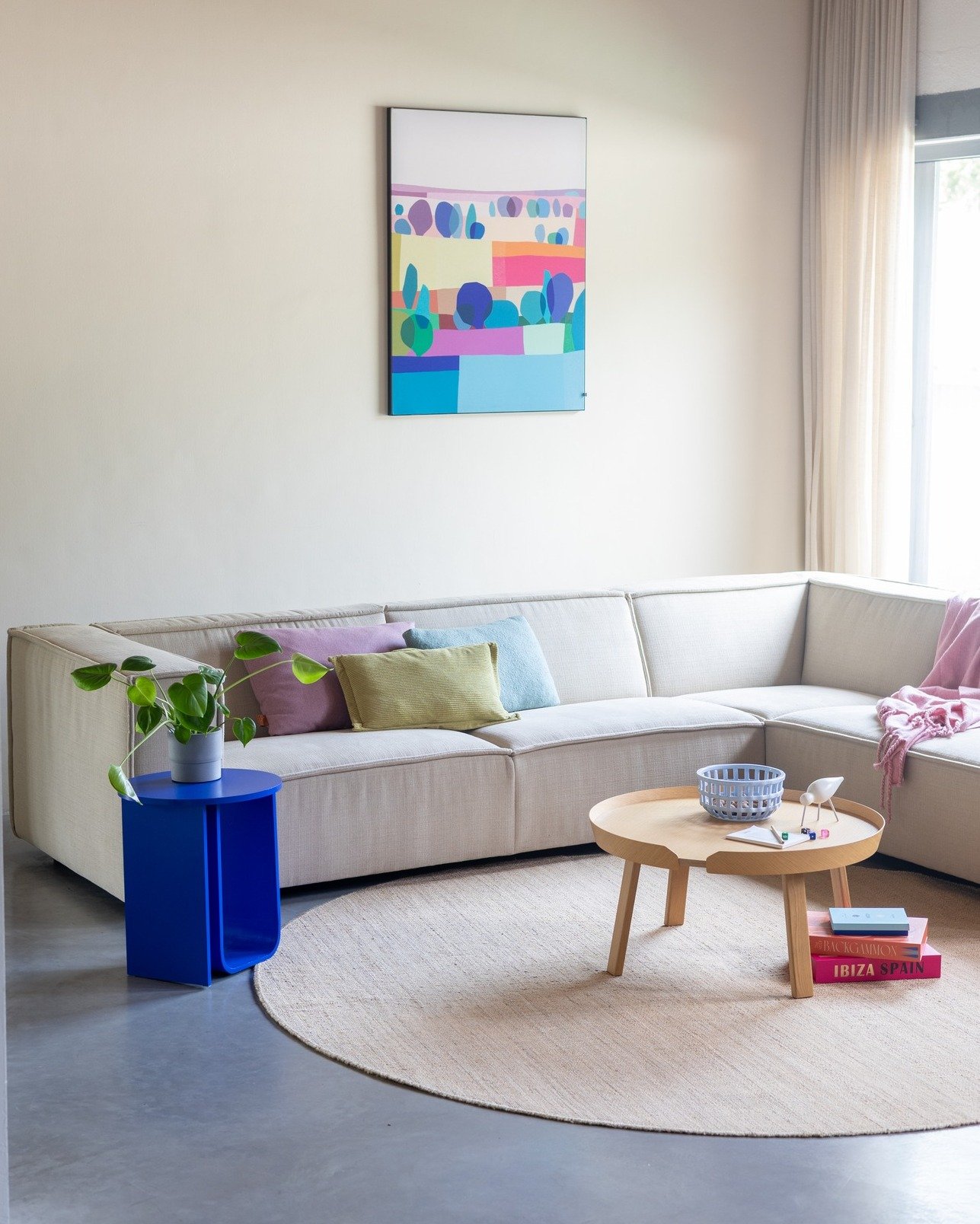 Beige fabric modular sofa on a round jute rug, with a cobalt blue side table and vibrant abstract art.