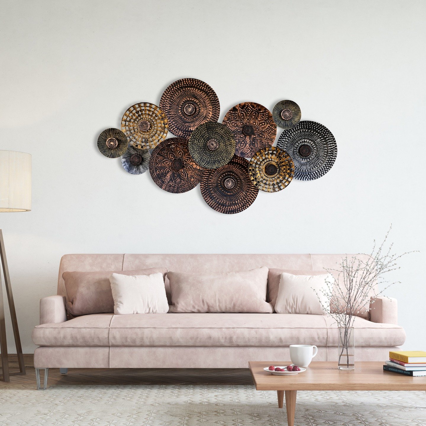 Cluster of overlapping circular metal wall sculptures in copper and bronze tones with mandala patterns, hung above a light pink sofa.