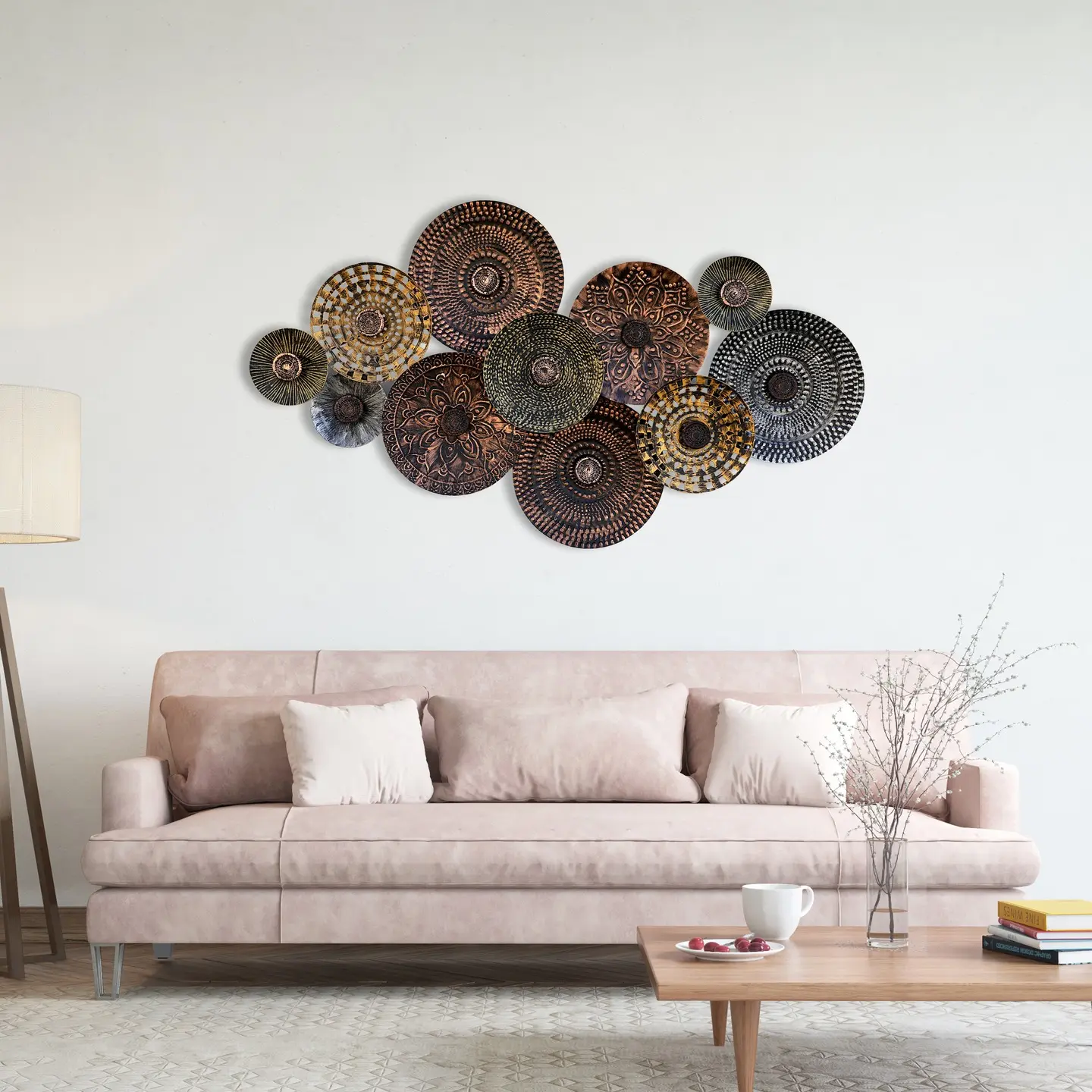 Cluster of overlapping circular metal wall sculptures in copper and bronze tones with mandala patterns, hung above a light pink sofa.