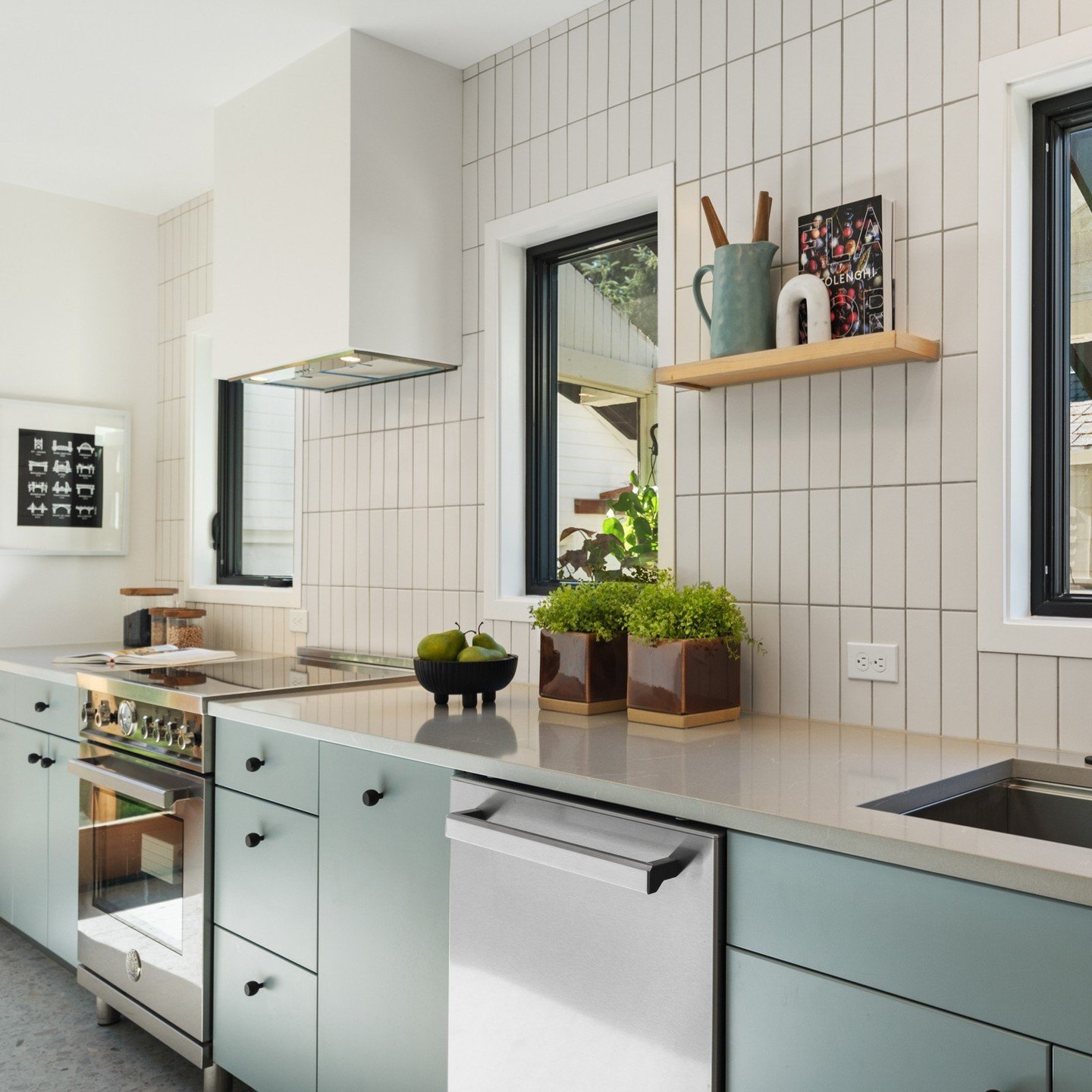 Contemporary kitchen with mint-green flat-panel cabinets, a white long vertical mosaic tile backsplash, a white box hood, and black-trimmed windows.