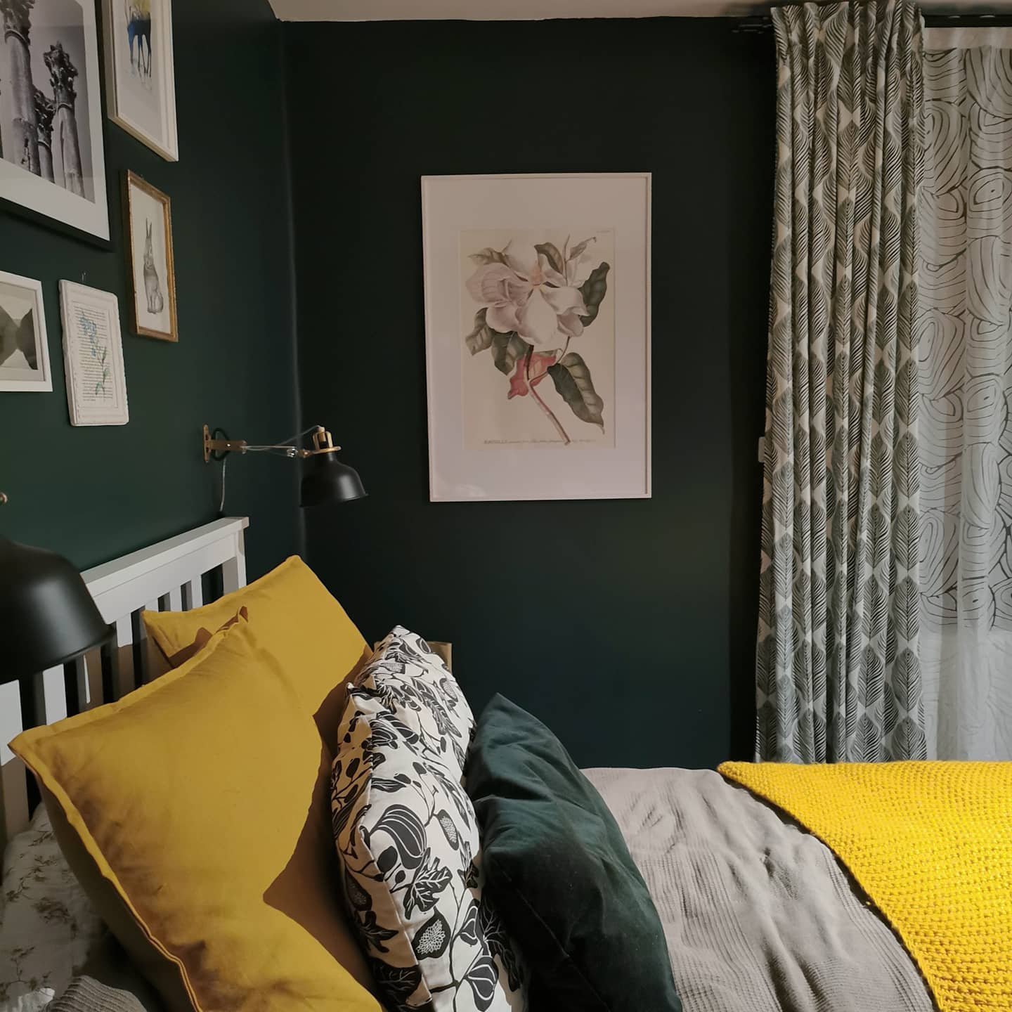 Bedroom corner with dark forest green walls, a white slatted headboard, and bedding featuring mustard yellow, grey, and floral patterns.