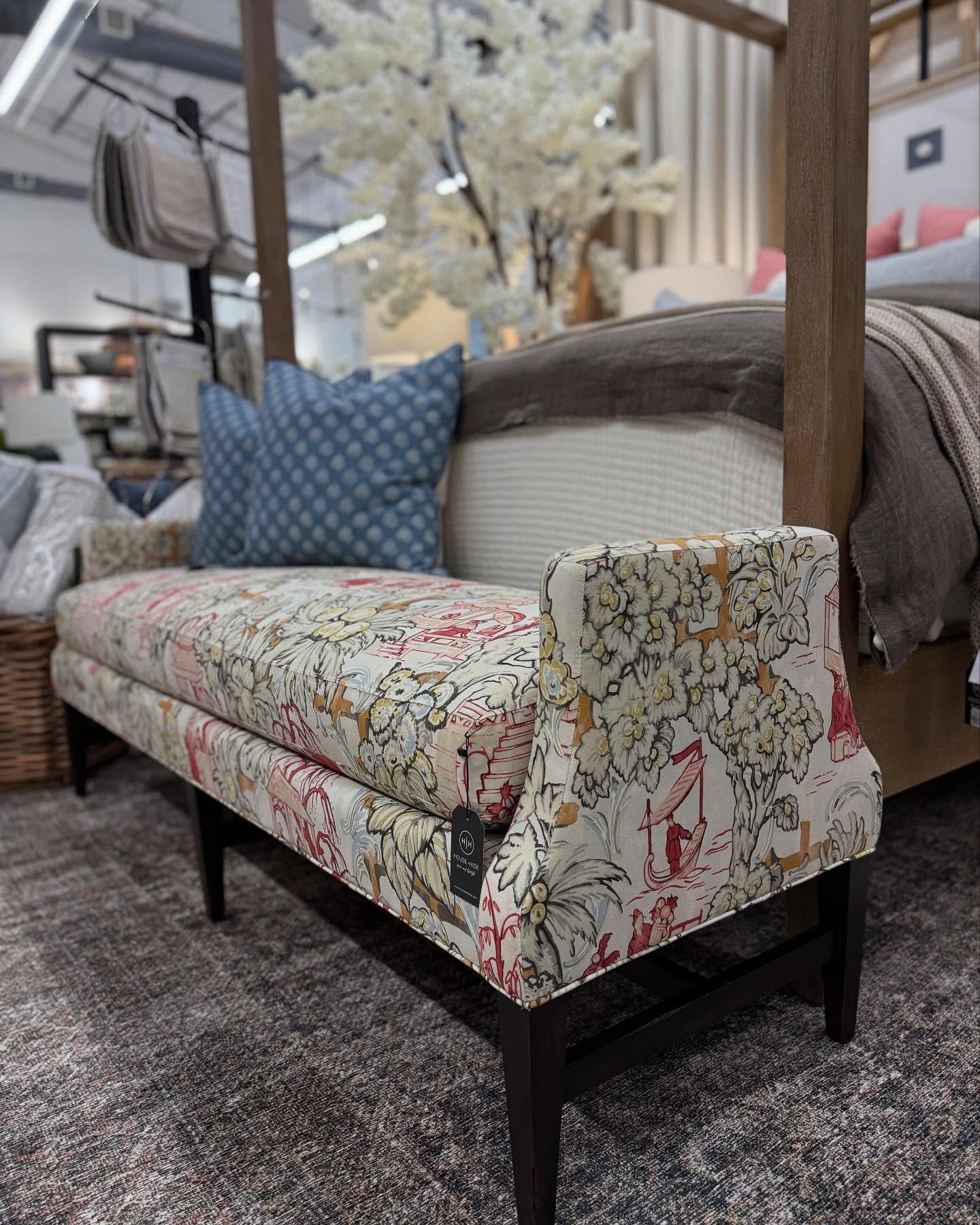 A small upholstered bedroom bench with short, sloped arms and dark legs, covered in a detailed multicolored scenic print fabric.