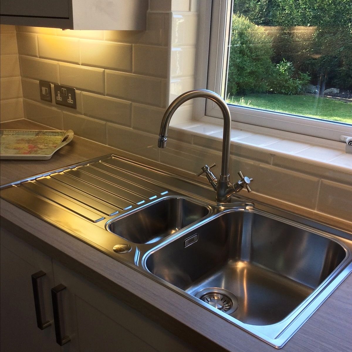 A top-down view of a traditional stainless steel drop-in (inset) sink featuring a large main bowl, a small second bowl, and an integrated draining board, with a chrome faucet.