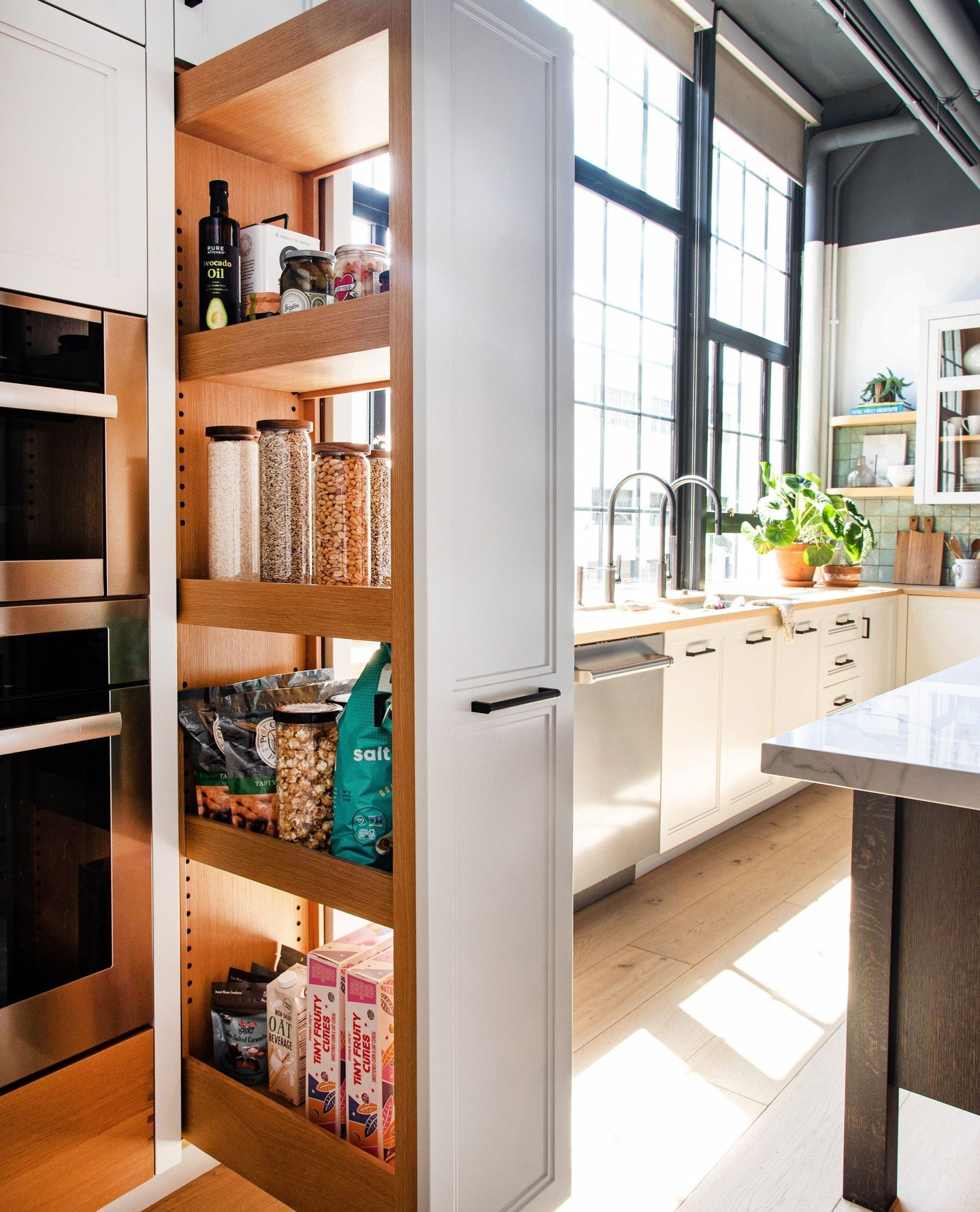 Tall, thin, full-extension pantry unit made of oak wood, pulled out to show dry goods, oils, and small pantry boxes.