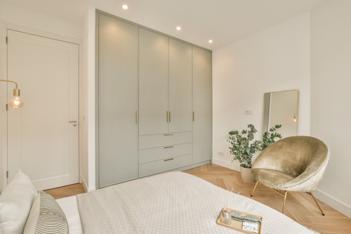 Built-in, floor-to-ceiling wardrobe in matte sage green featuring a bank of central drawers and slim brass bar handles in a contemporary bedroom.