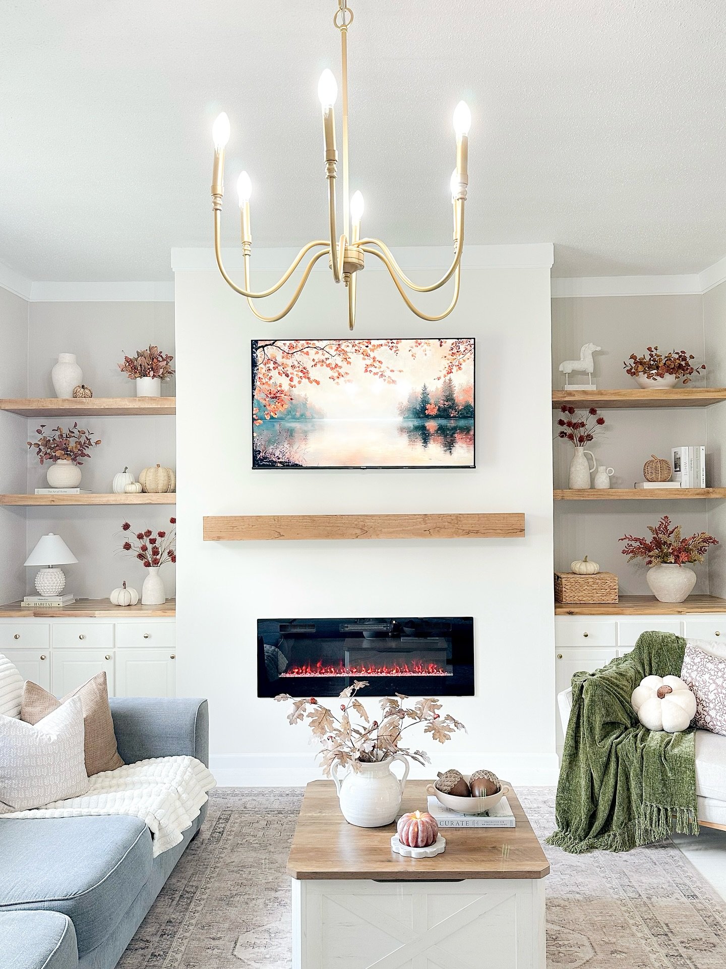 Bright living room with a linear electric fireplace, wood beam mantel, and symmetrical white built-in cabinets with natural wood floating shelves.