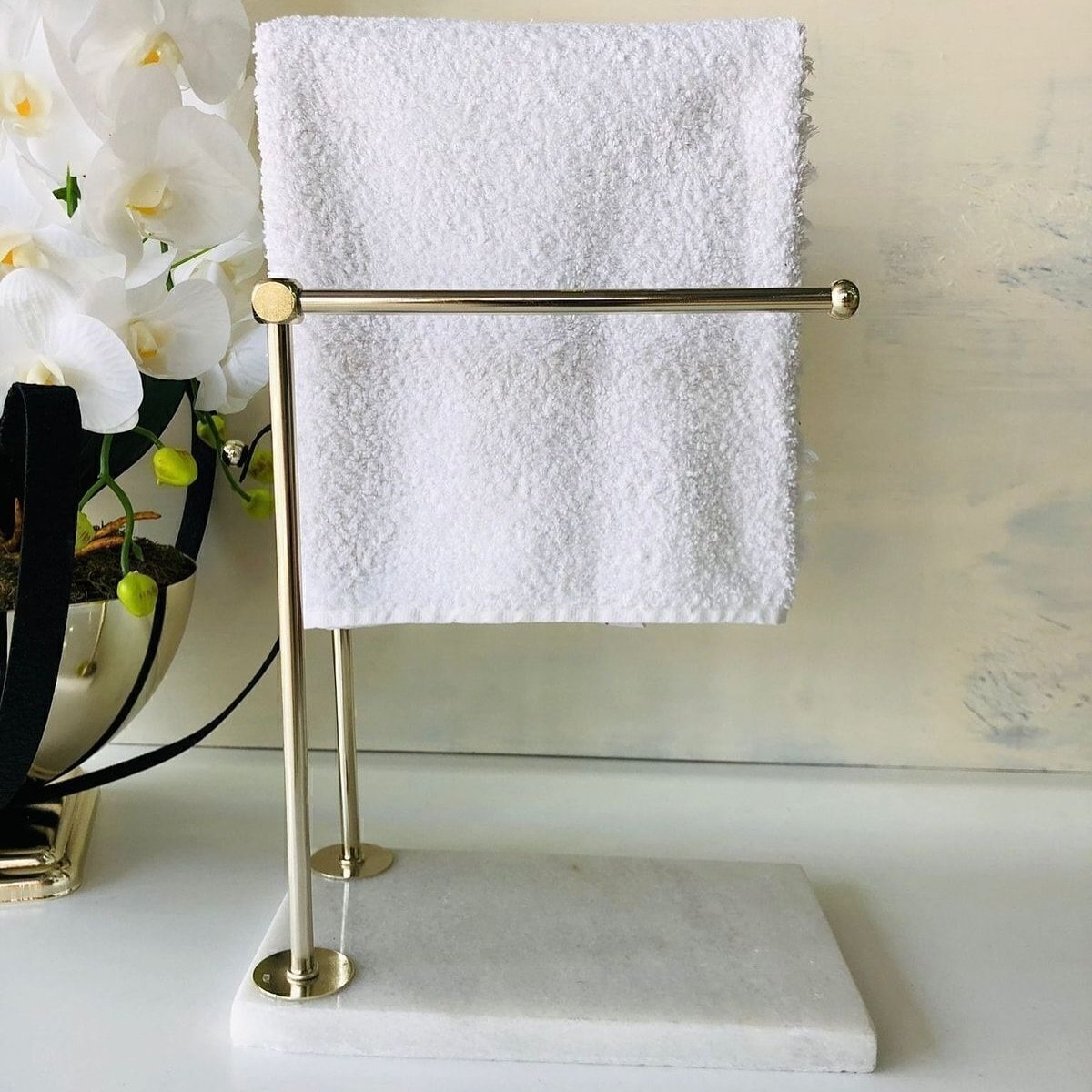 Close-up of a small, polished brass countertop towel holder with a rectangular white marble base, displaying a folded white hand towel.