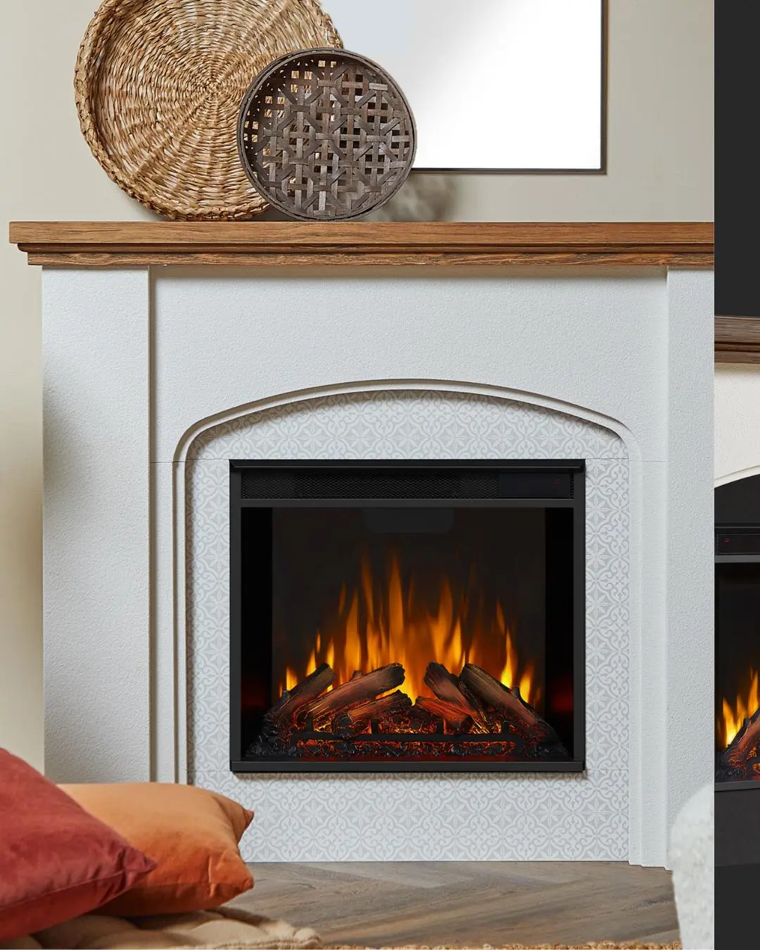 White electric fireplace mantel with a wooden top, featuring a faux arch design around the firebox, which has a stenciled patterned background and realistic glowing logs.