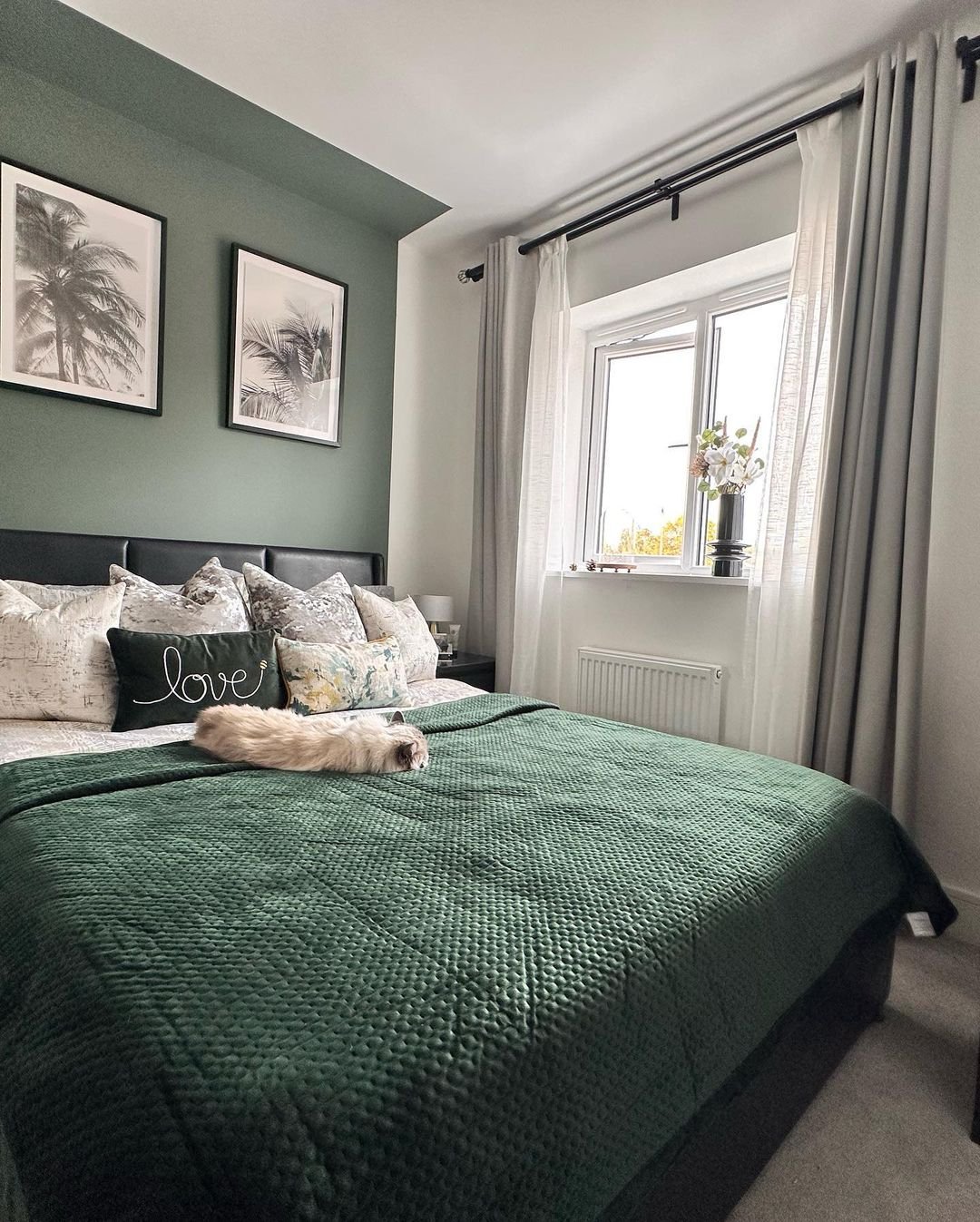 Modern bedroom with a deep sage green accent wall, black leather headboard, and a quilted dark green bedspread.