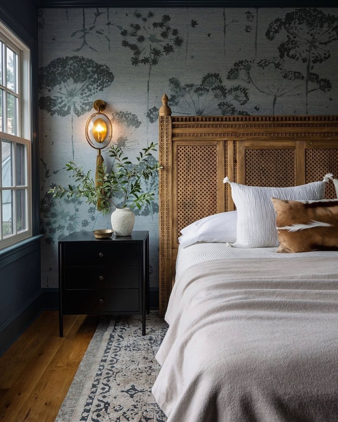 Simple black nightstand with two drawers and thin metal legs, next to a detailed wooden carved and cane headboard.