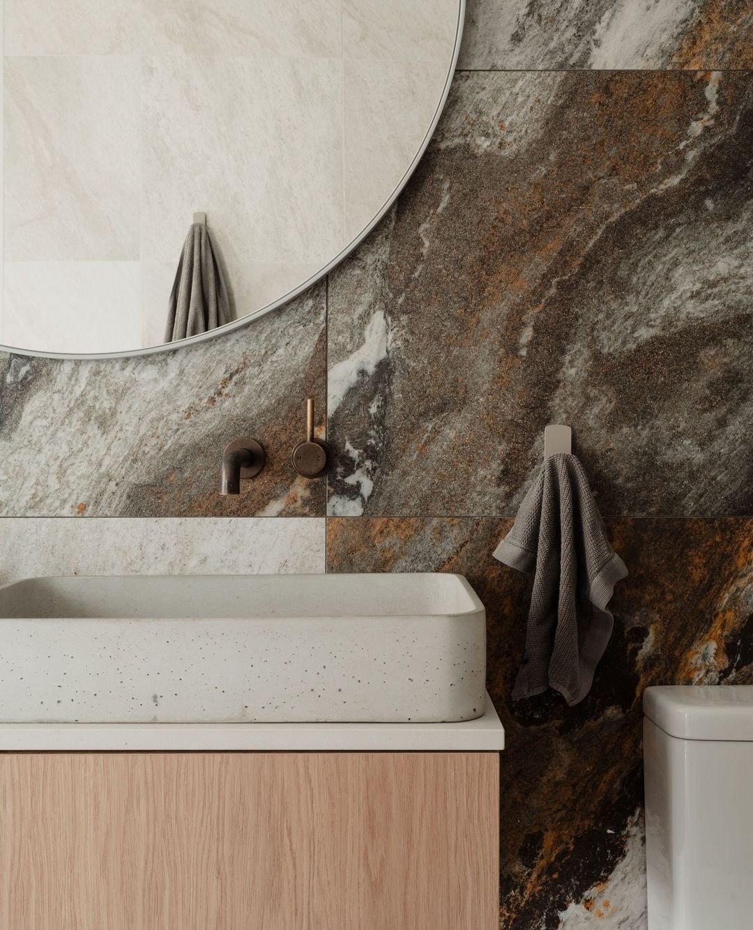 A small, square, off-white peg hook holding a dark gray waffle-weave hand towel against a dramatic brown and white marble wall.